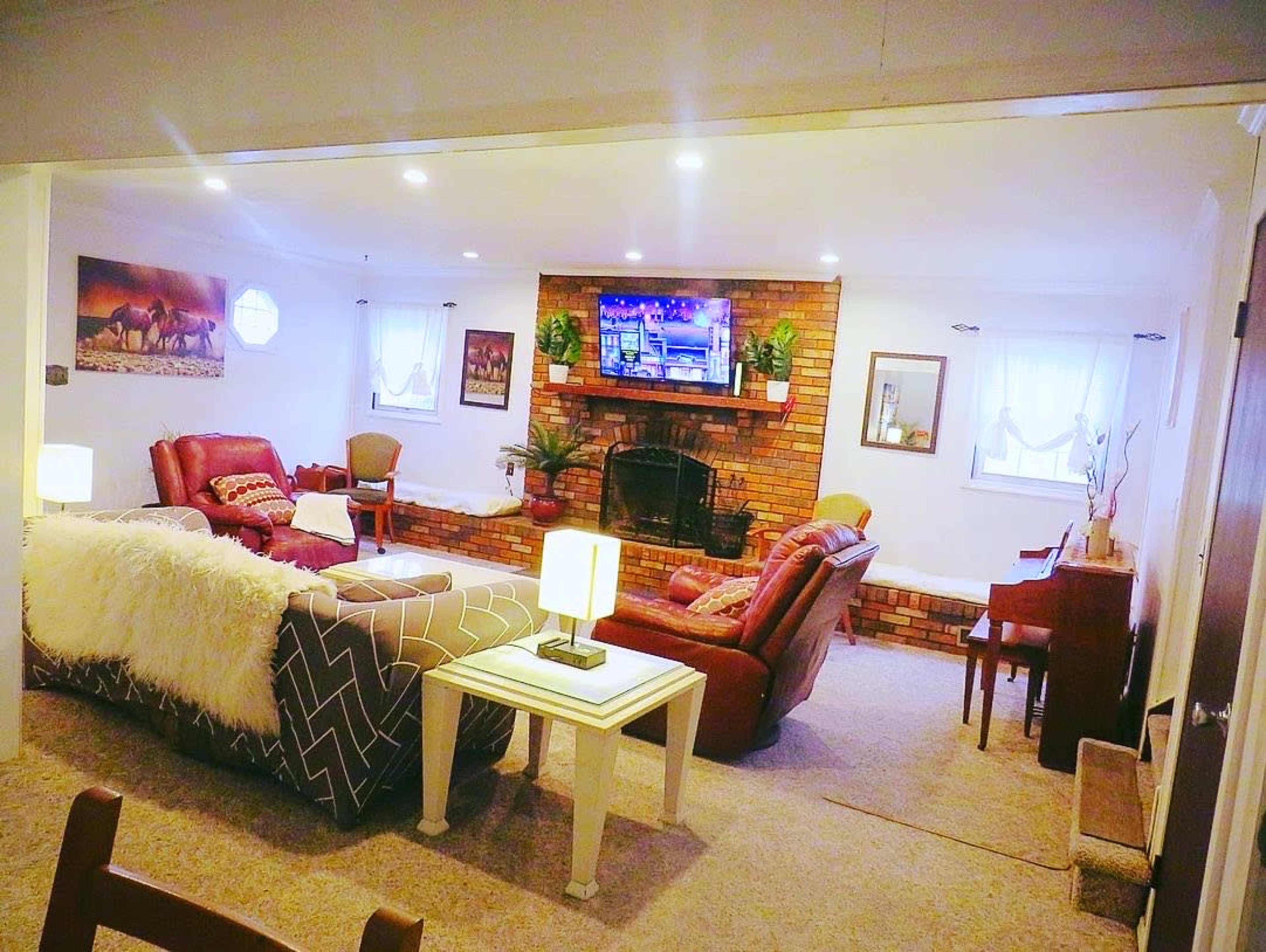A cozy living room with a brick wall, a television mounted above a fireplace, and seating arranged around a small table.