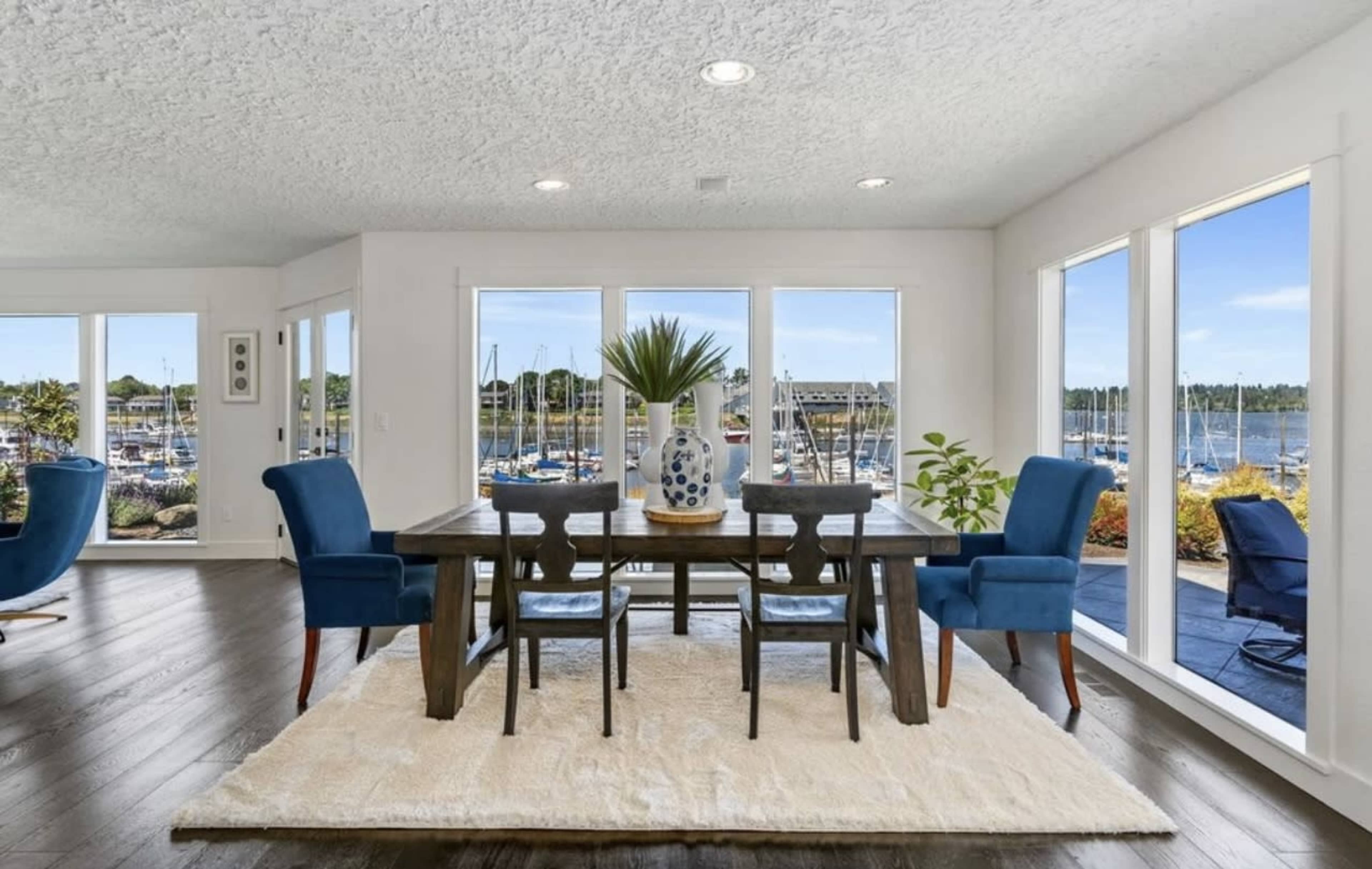 A dining area with a wooden table surrounded by blue chairs, located near large windows that provide a view of a marina.