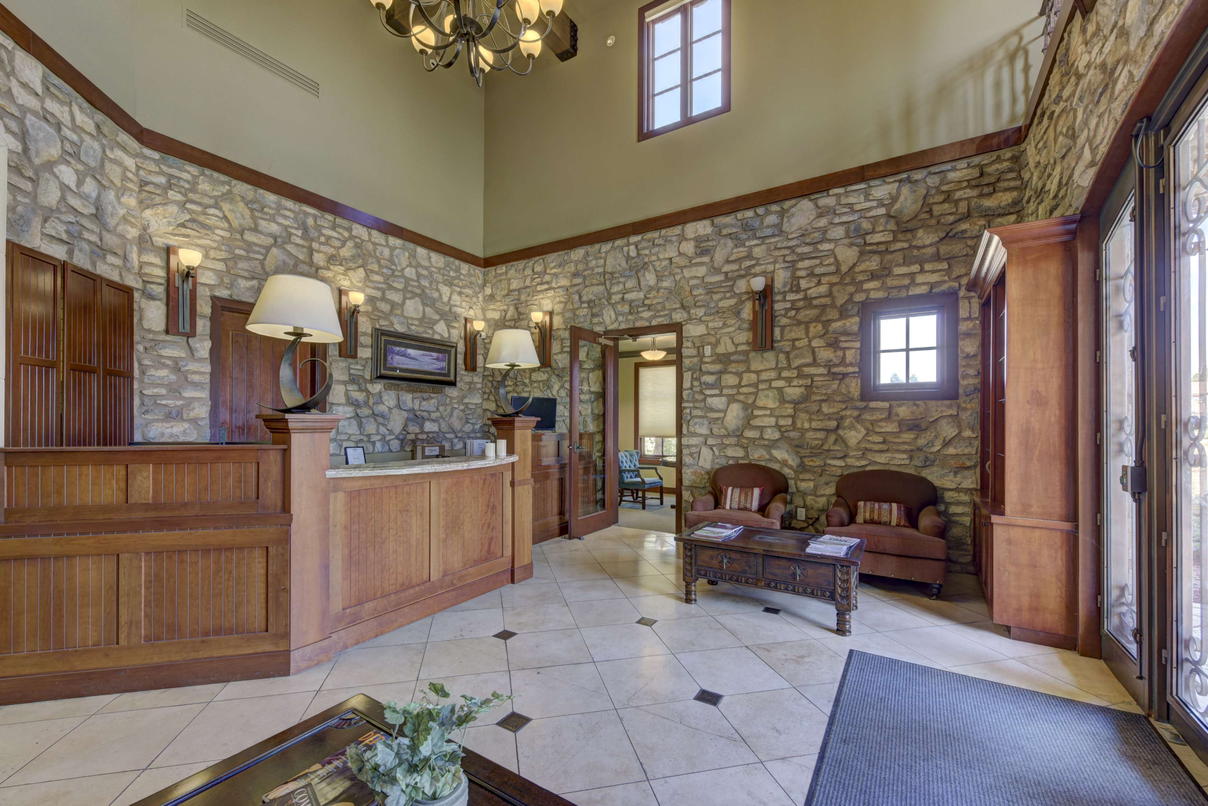 A spacious lobby with stone walls, wooden accents, a reception desk, and a seating area featuring two chairs and a coffee table.