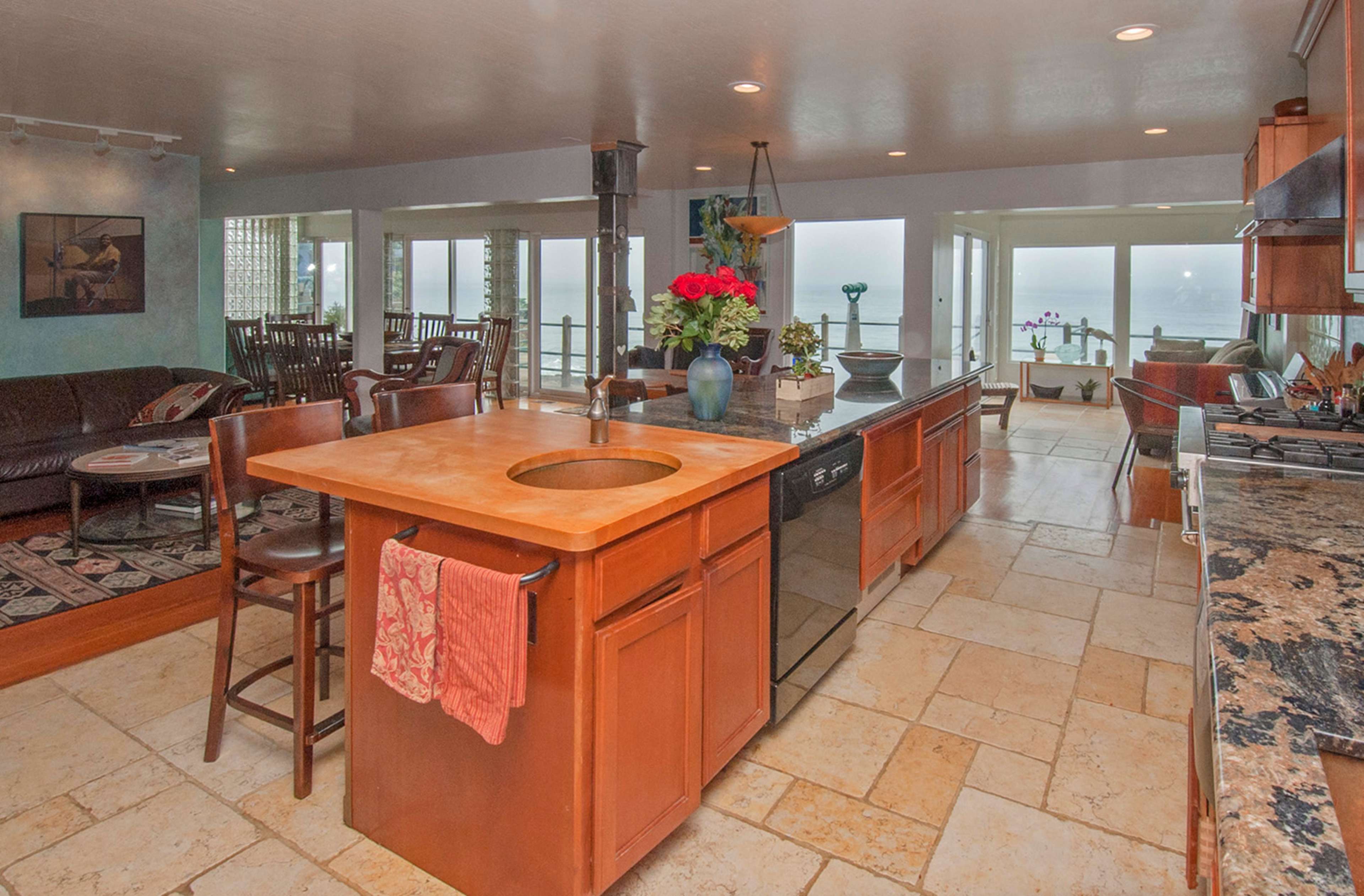 A kitchen with an island, wooden stools, and large windows overlooking a body of water.
