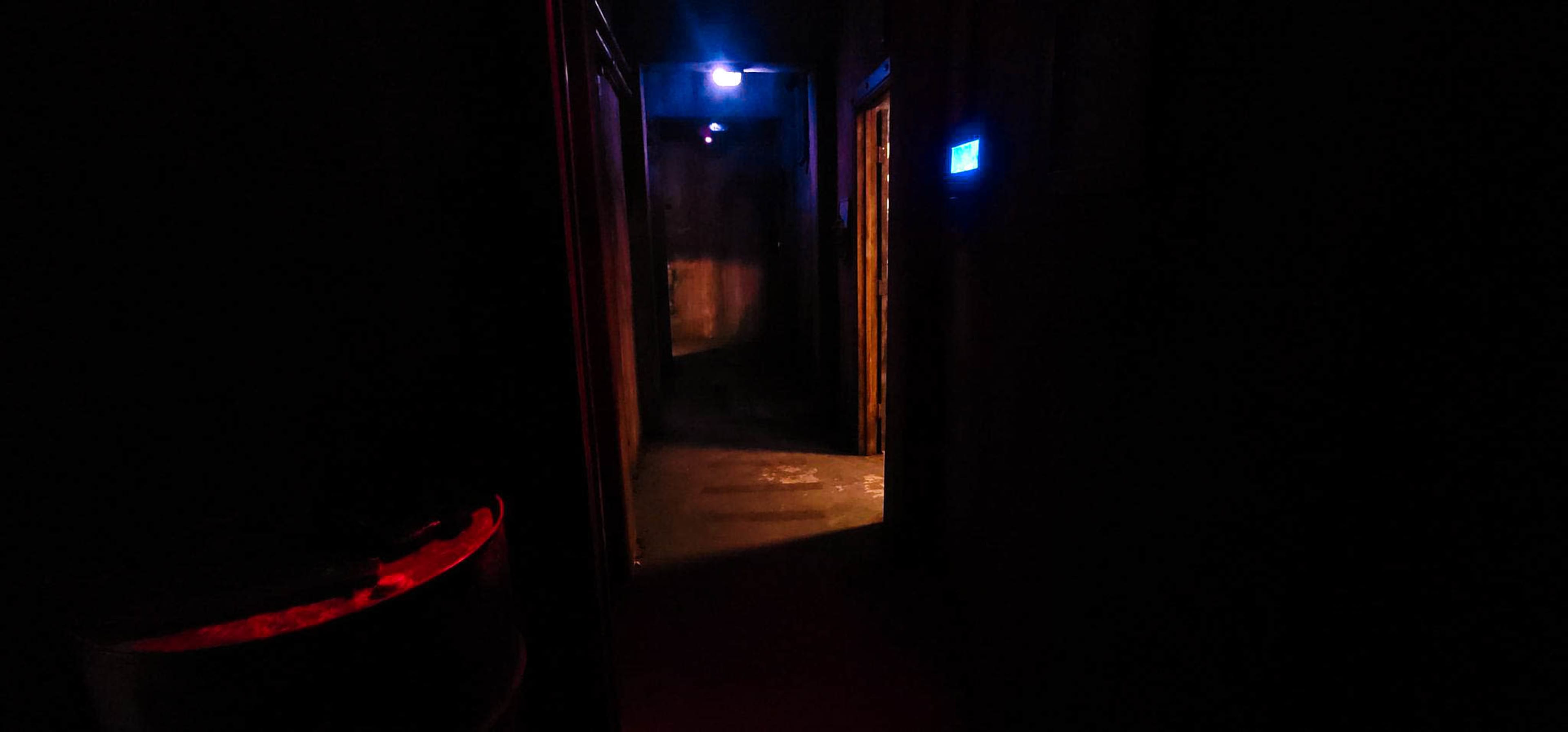 The image shows a dimly lit hallway with faint blue and red lights at either end, leading to closed doors on each side.