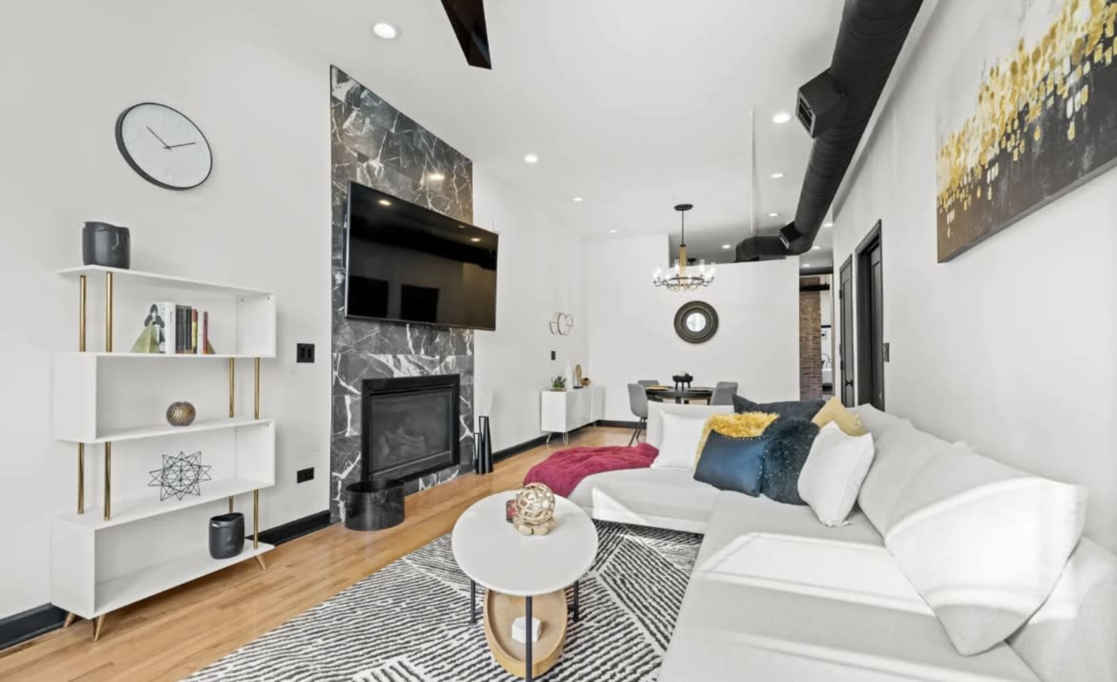 A modern living room features a sleek sofa, a marble fireplace, and a large wall-mounted television.