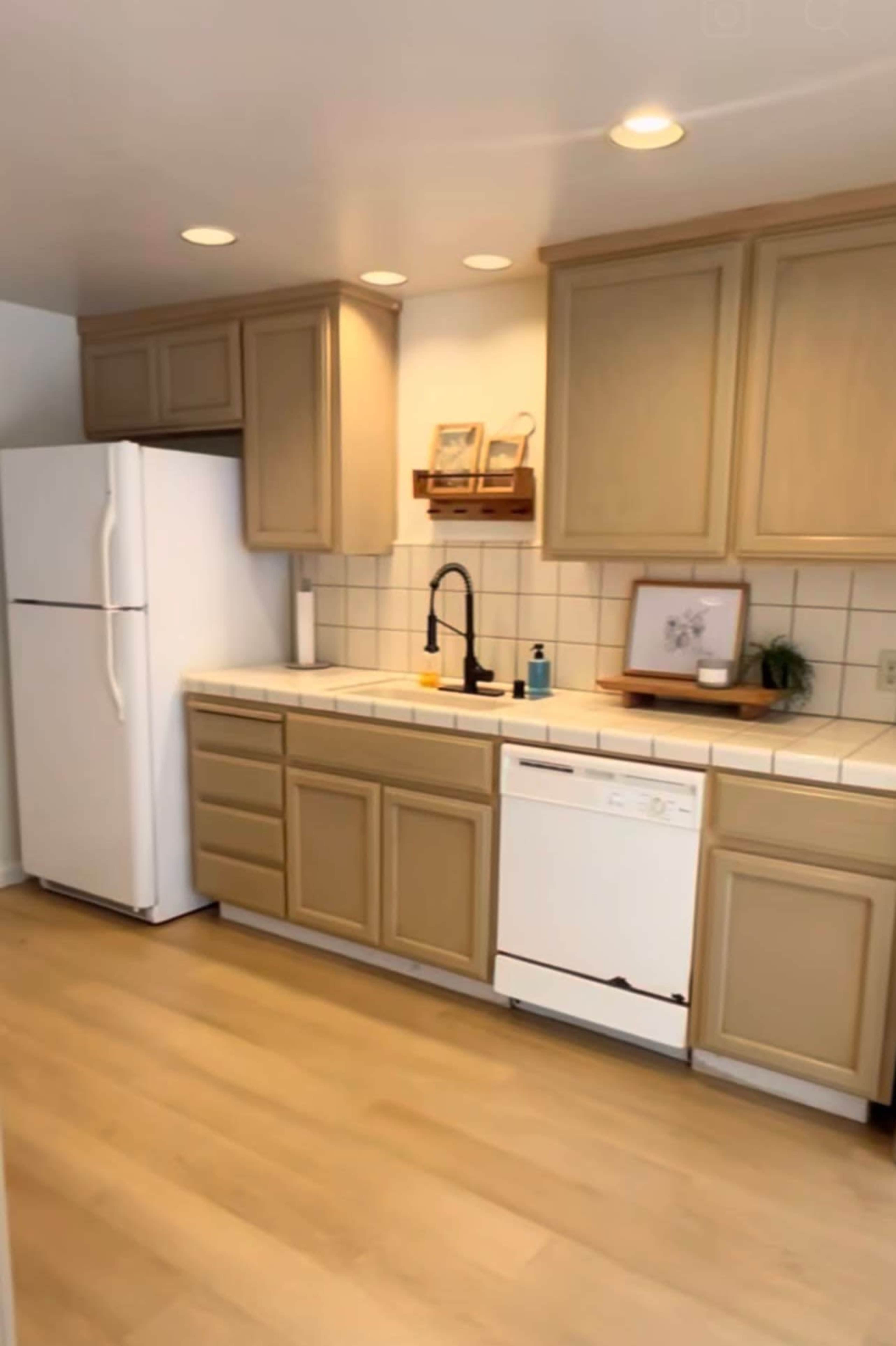 The kitchen features beige cabinets, a white refrigerator, and a sink area with a black faucet, along with a dishwasher and tiled countertops.