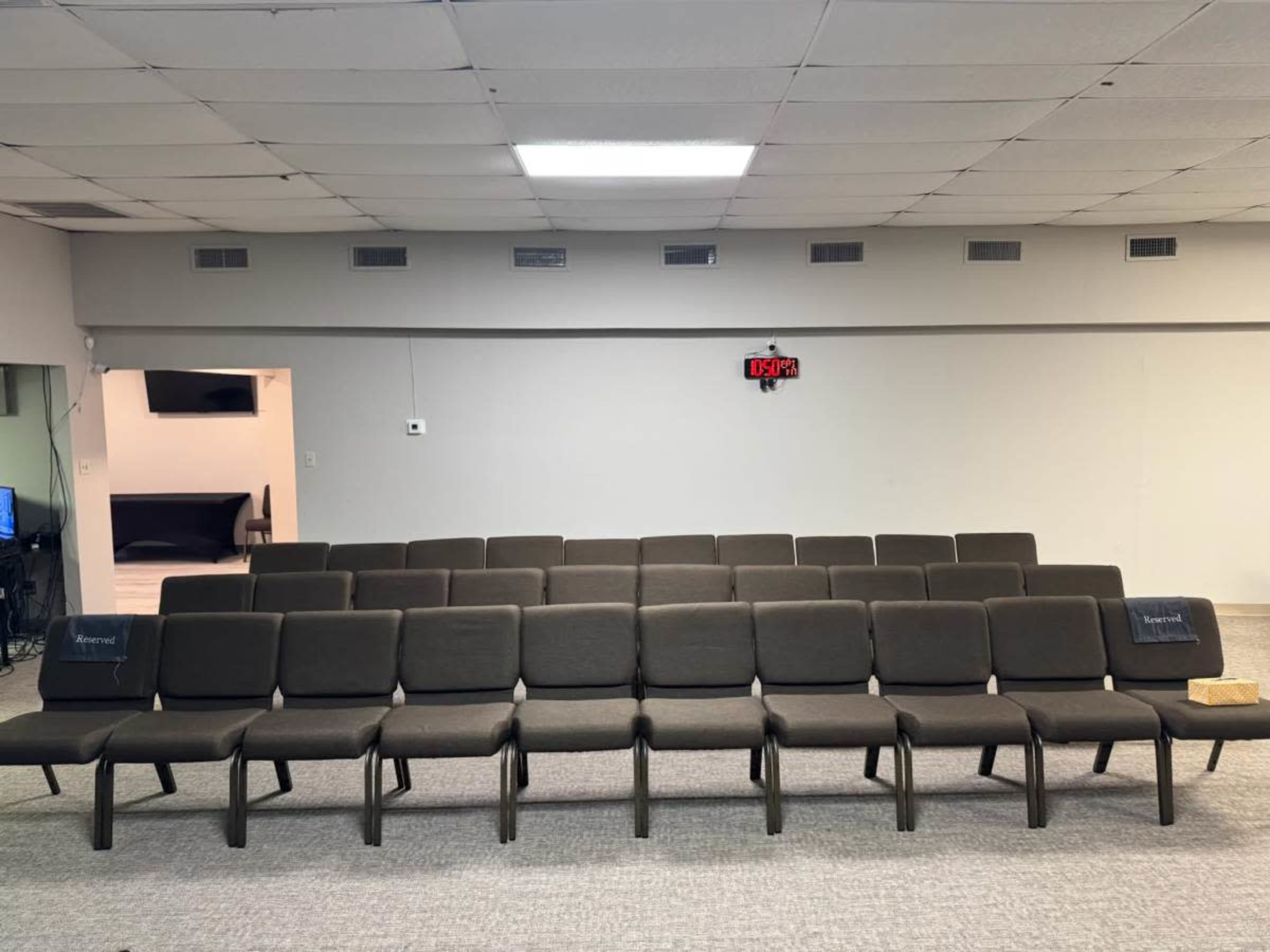 A row of gray upholstered chairs is arranged neatly in a spacious, well-lit room with a clock on the wall.