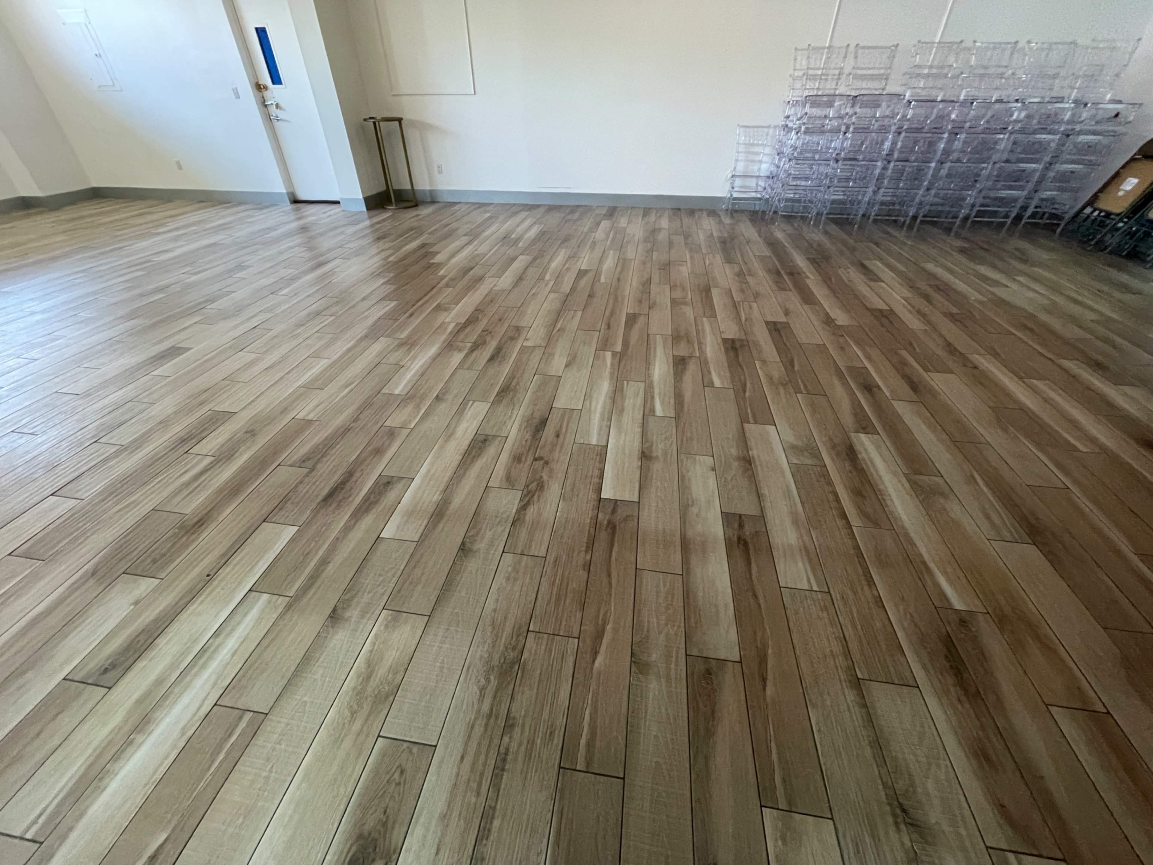 A spacious room with wooden flooring arranged in a herringbone pattern and storage racks in the background.