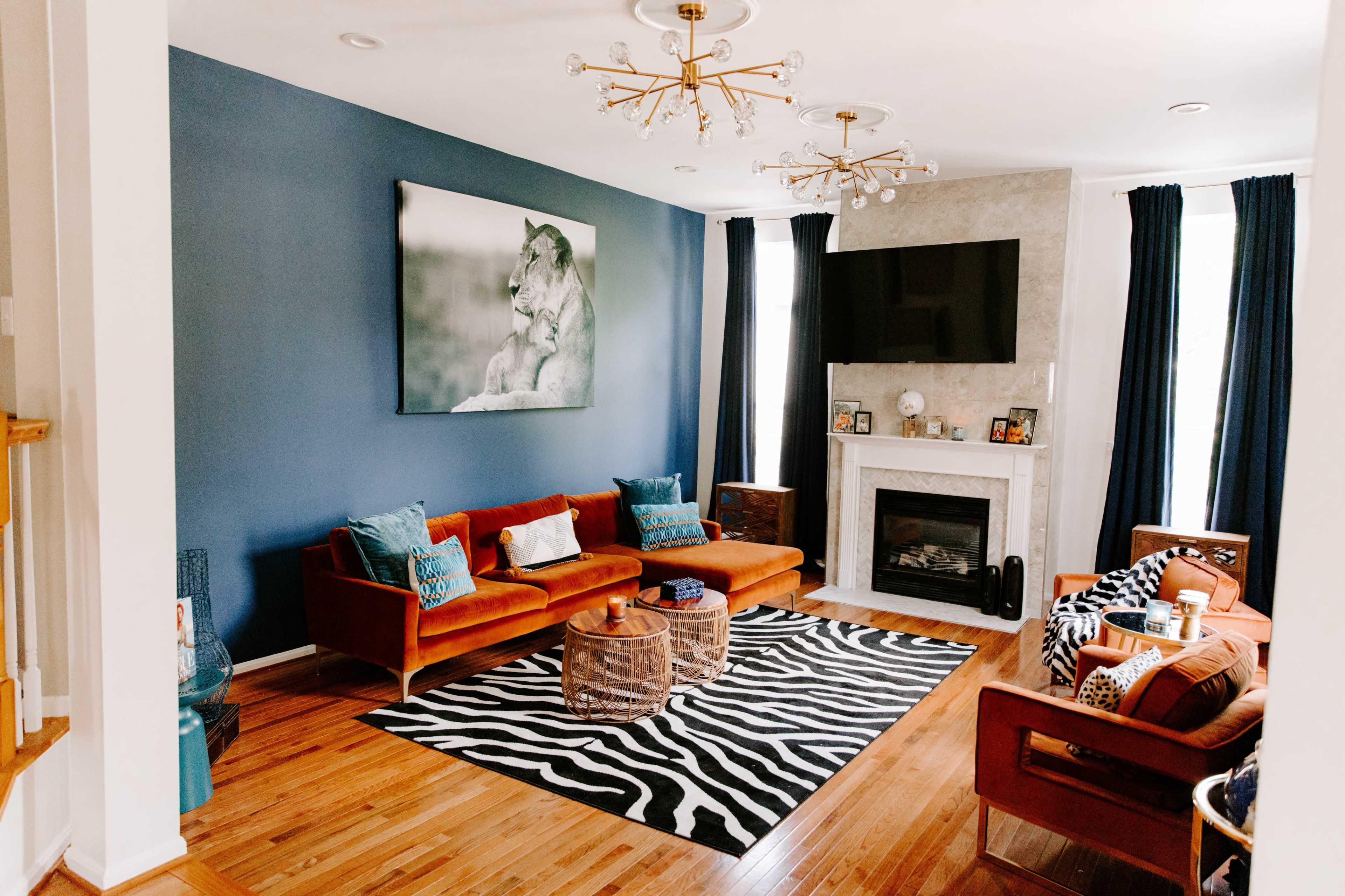 The living room features a blue accent wall, a stone fireplace, two sets of seating, and a zebra-patterned rug.