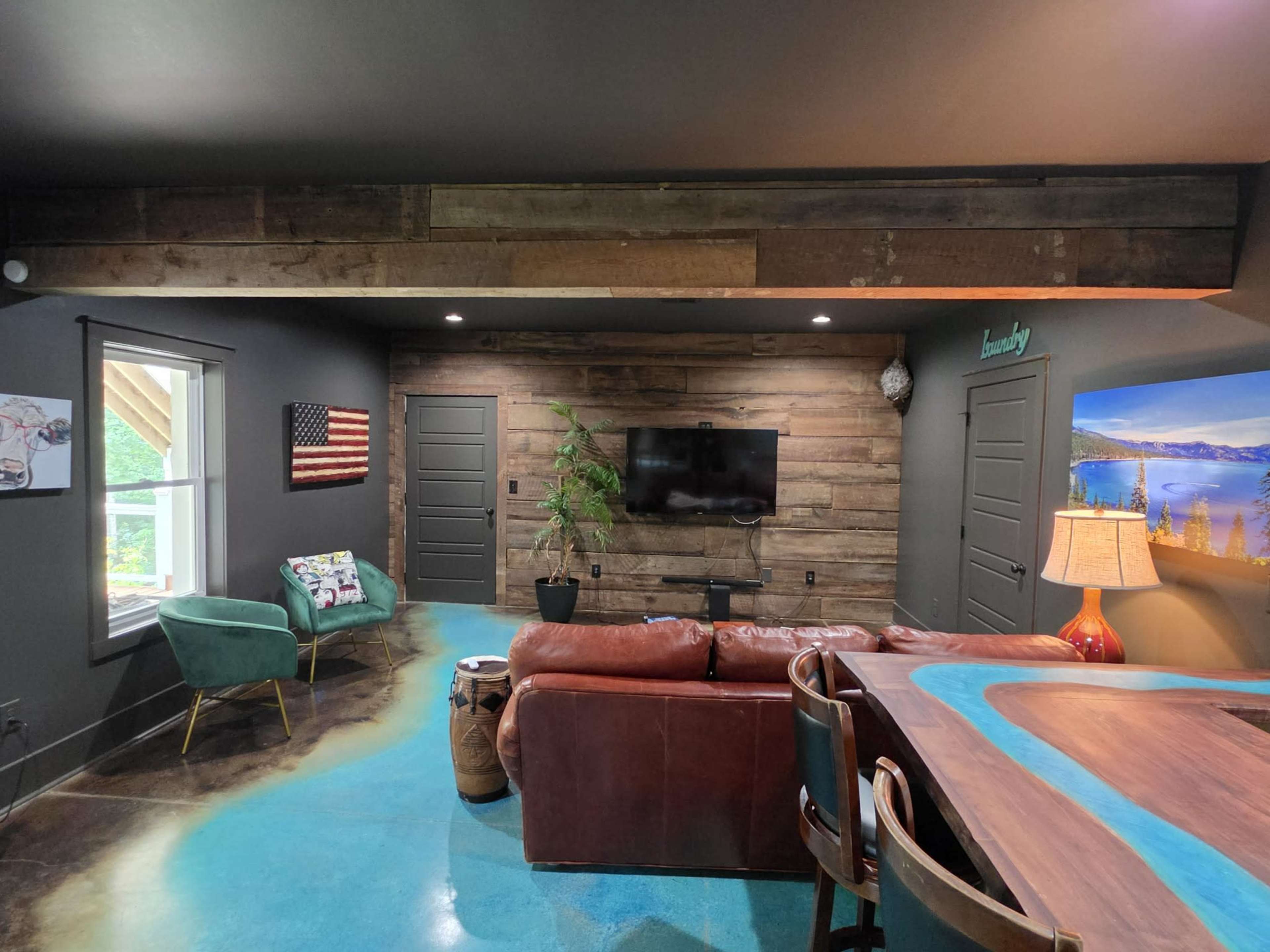 The image shows a cozy living space with a leather sofa, a wooden accent wall featuring a TV, and a turquoise epoxy floor.