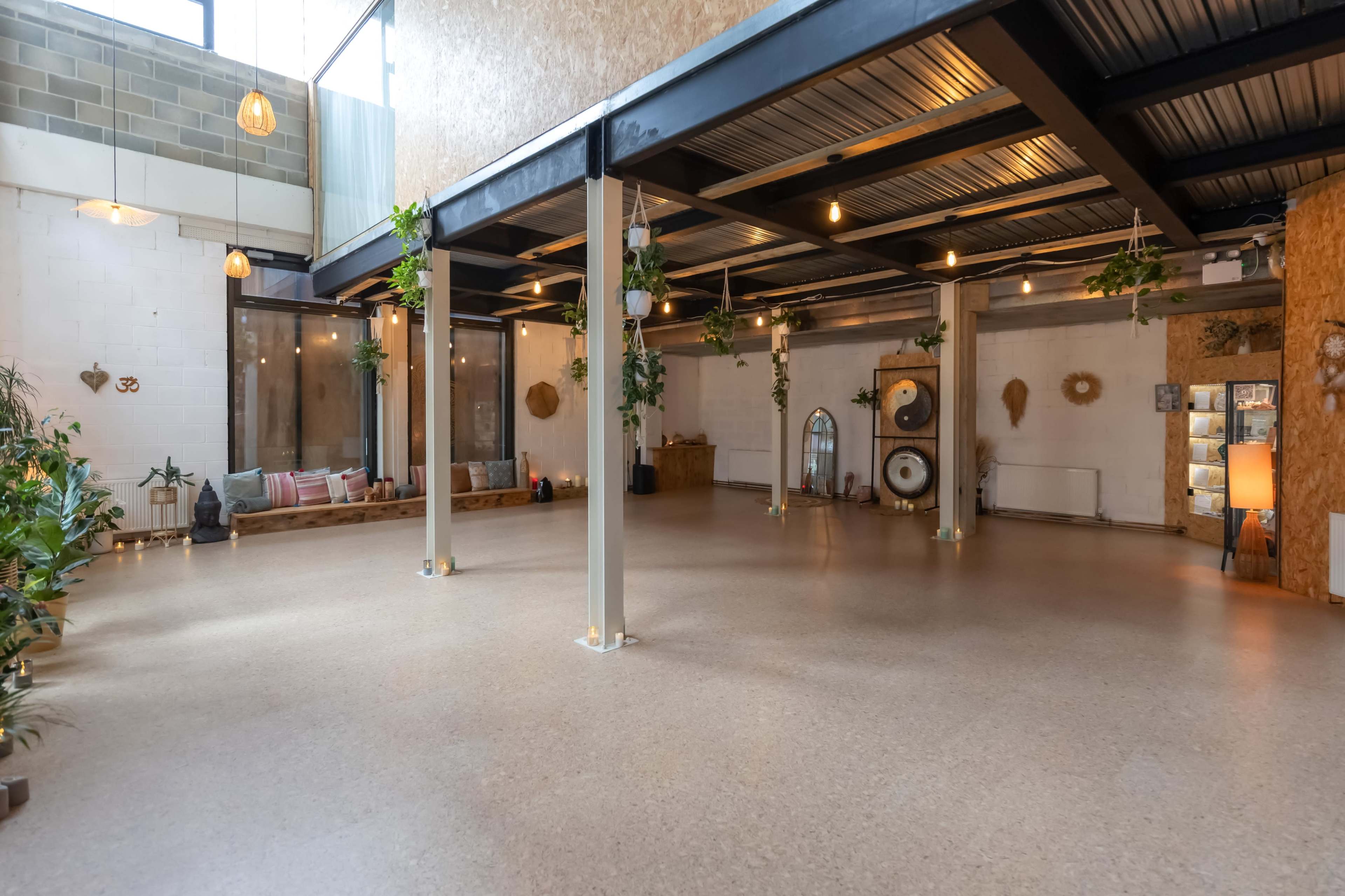 The image shows a spacious indoor venue with a polished floor, large windows, and various plants, featuring a minimalist decor style.