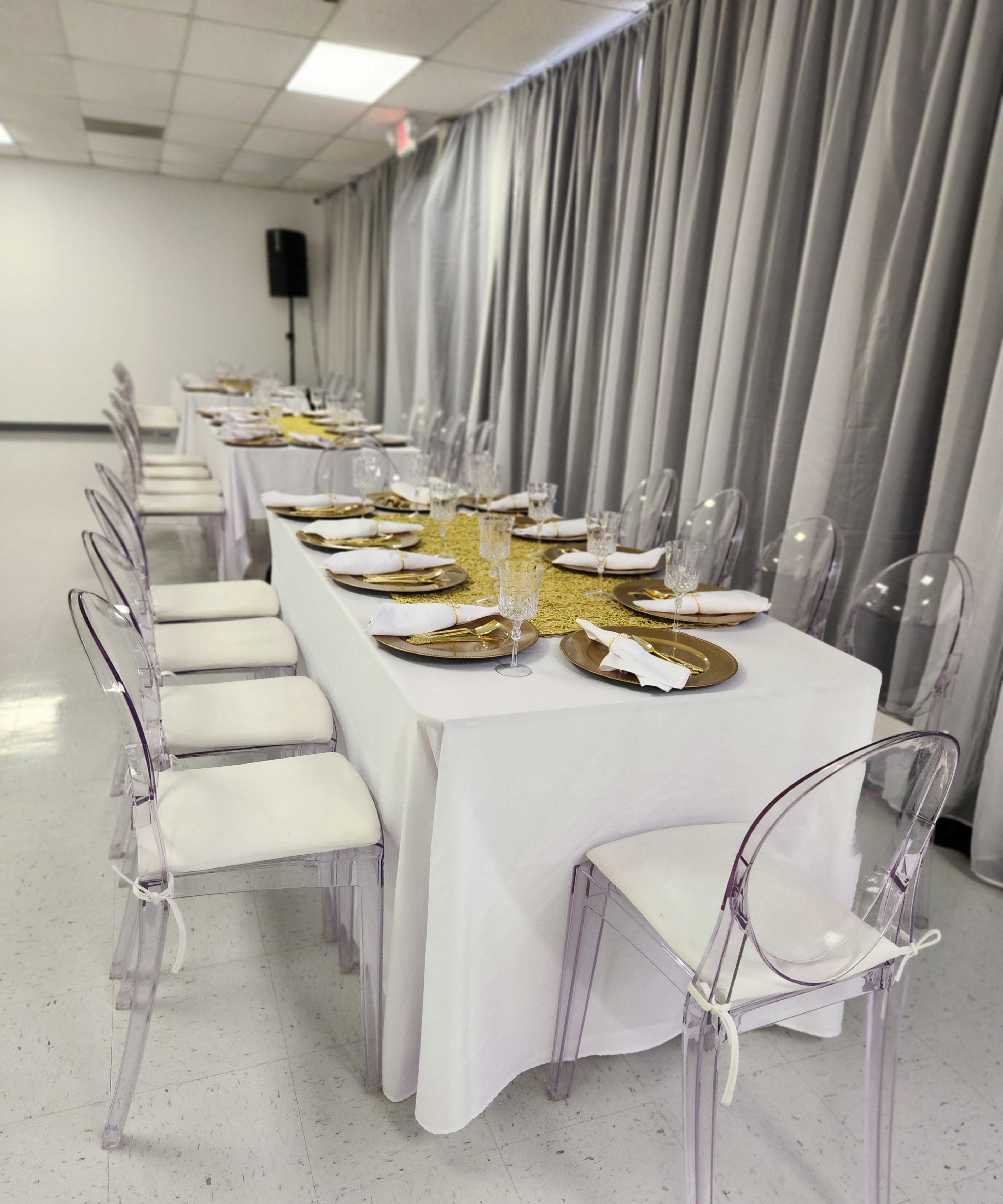 A long dining table is set with golden plates and glassware in a room with gray curtains.