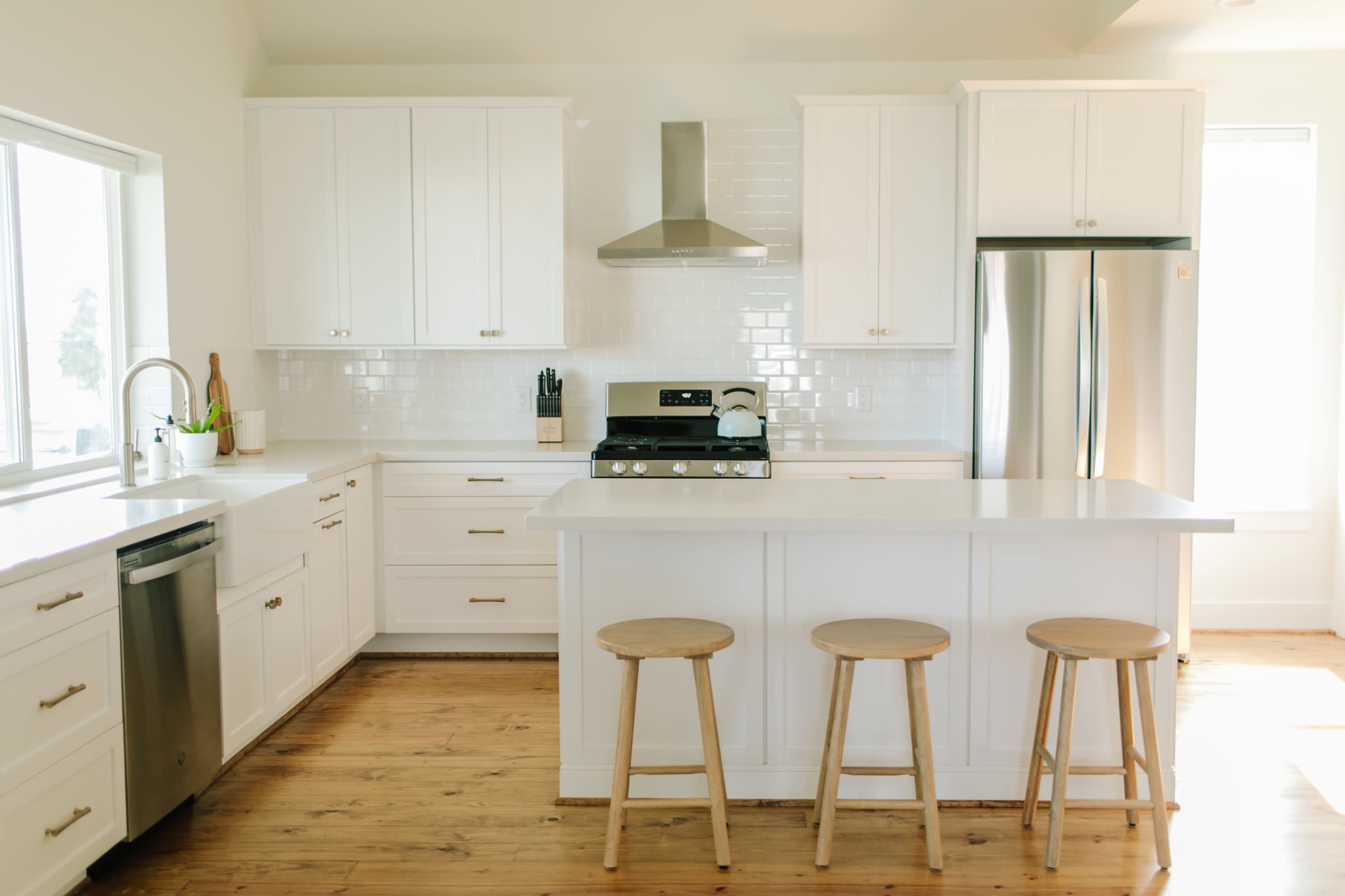 A modern kitchen features white cabinetry, stainless steel appliances, and three wooden stools at a central island.
