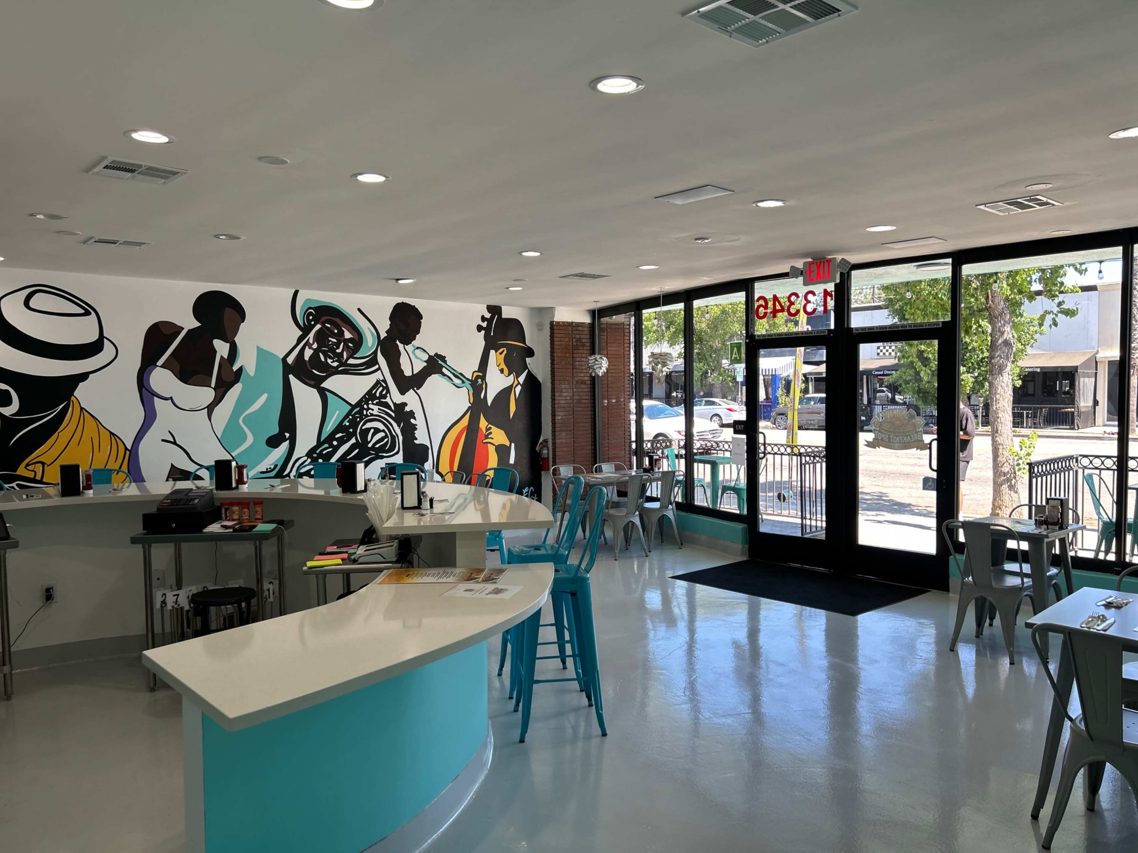 The interior of a café features colorful wall murals and a bright, open seating area with tables and chairs.
