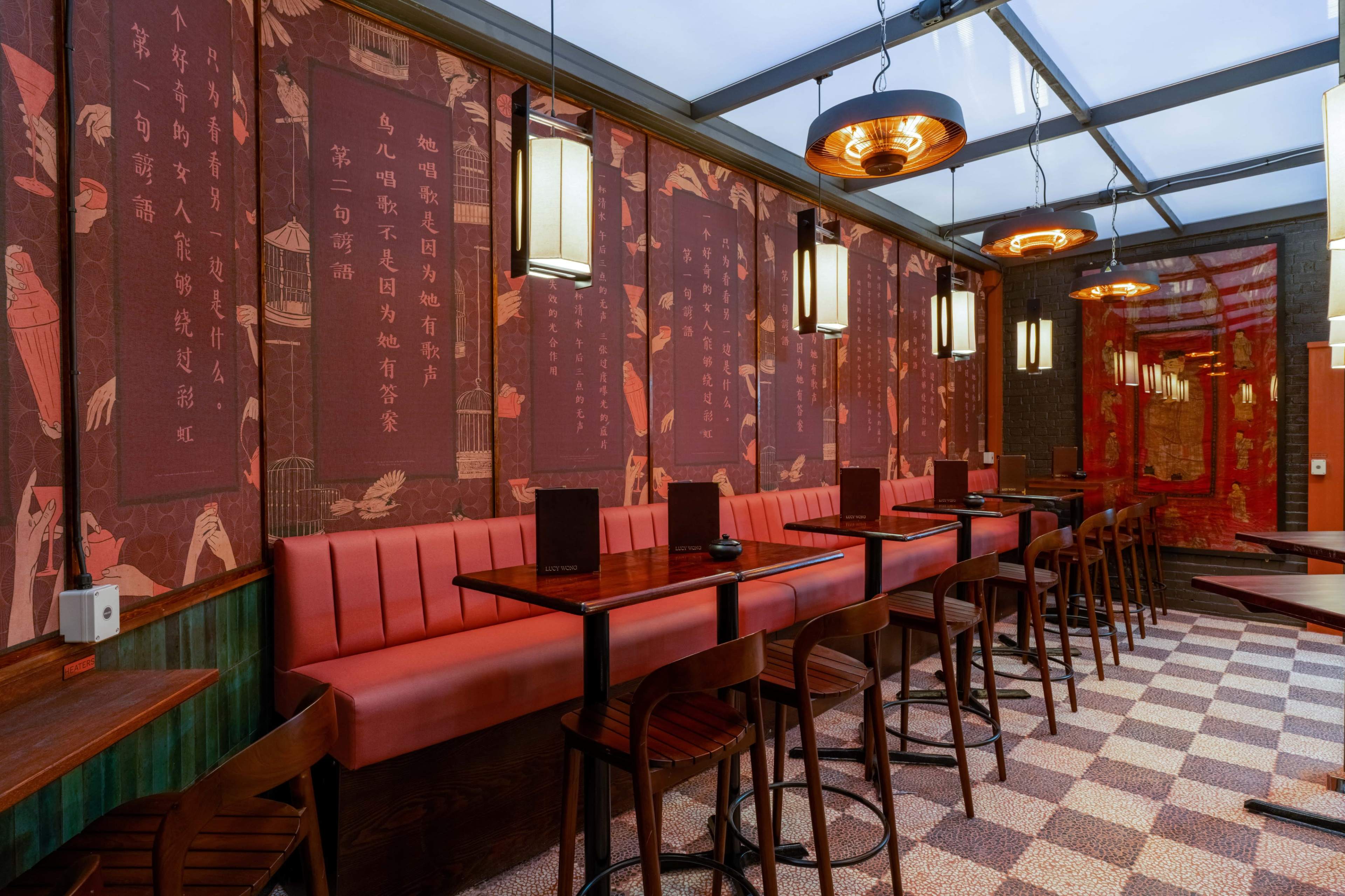 The image shows a restaurant interior featuring red walls adorned with traditional Chinese calligraphy, a row of wooden tables and high chairs, and pendant lighting above the seating area.