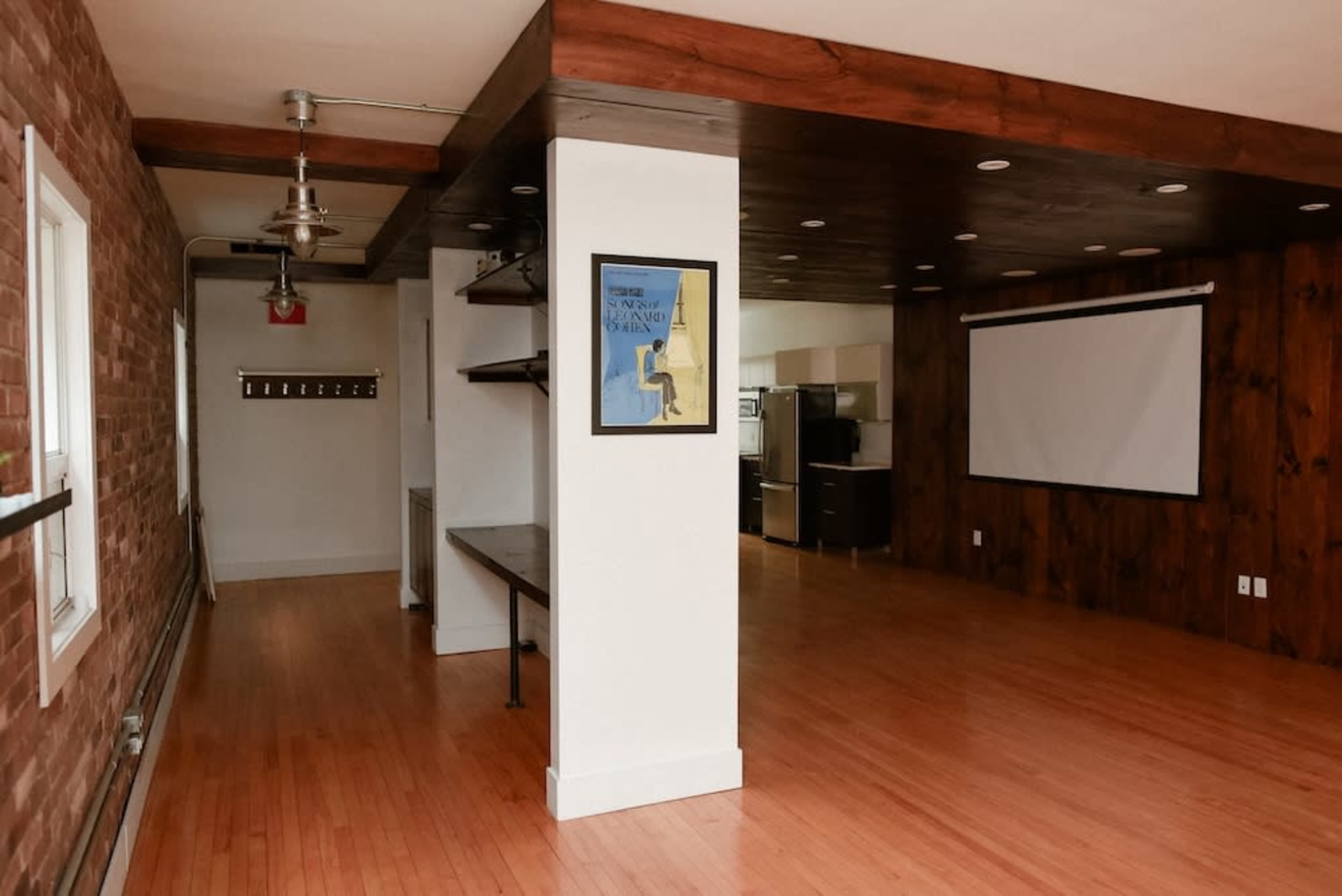 The image shows a spacious room with hardwood floors, a bright wall, a wooden ceiling, and a large wall screen.