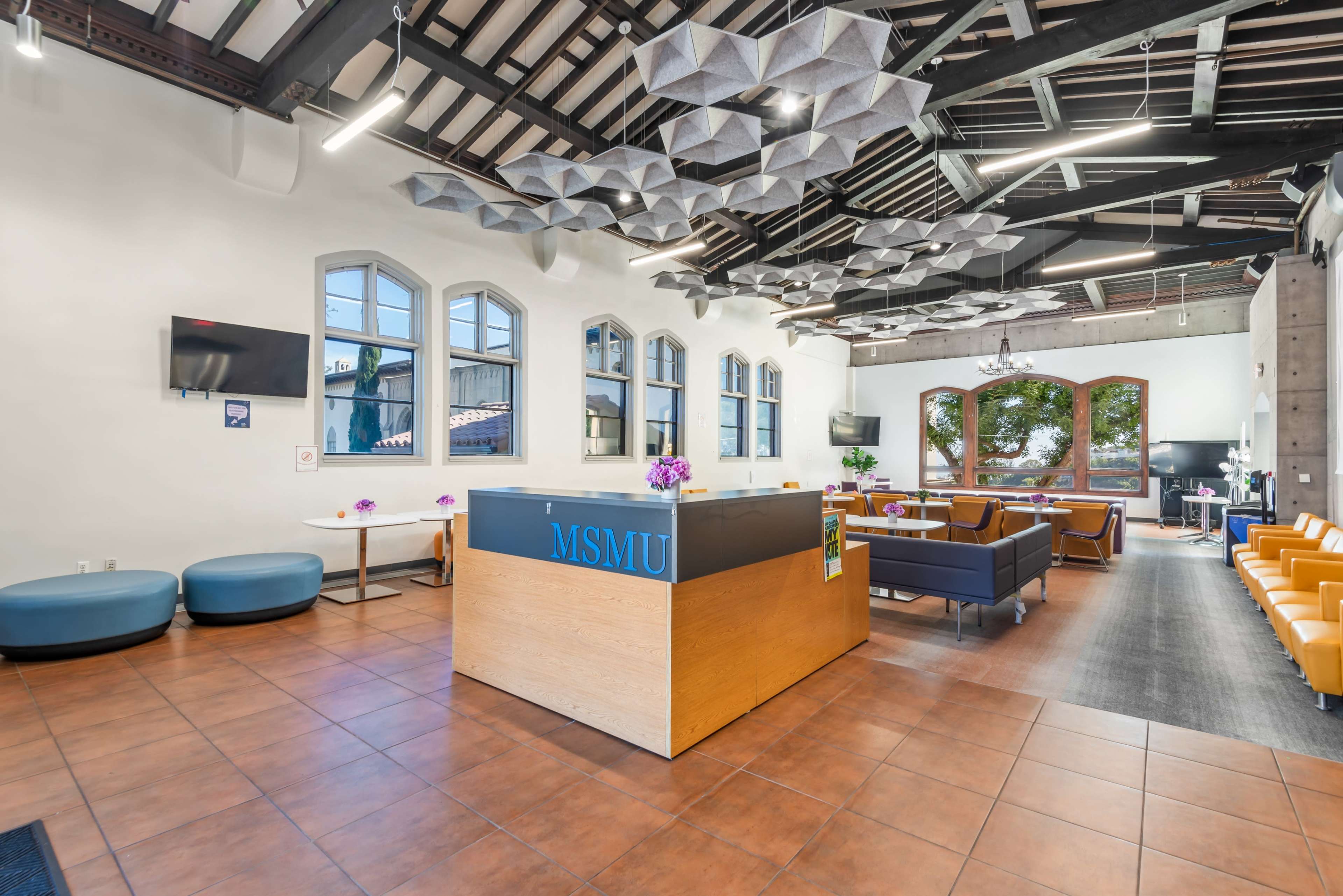 The image shows a modern reception area with a wooden front desk, seating arrangements, and decorative ceiling features.