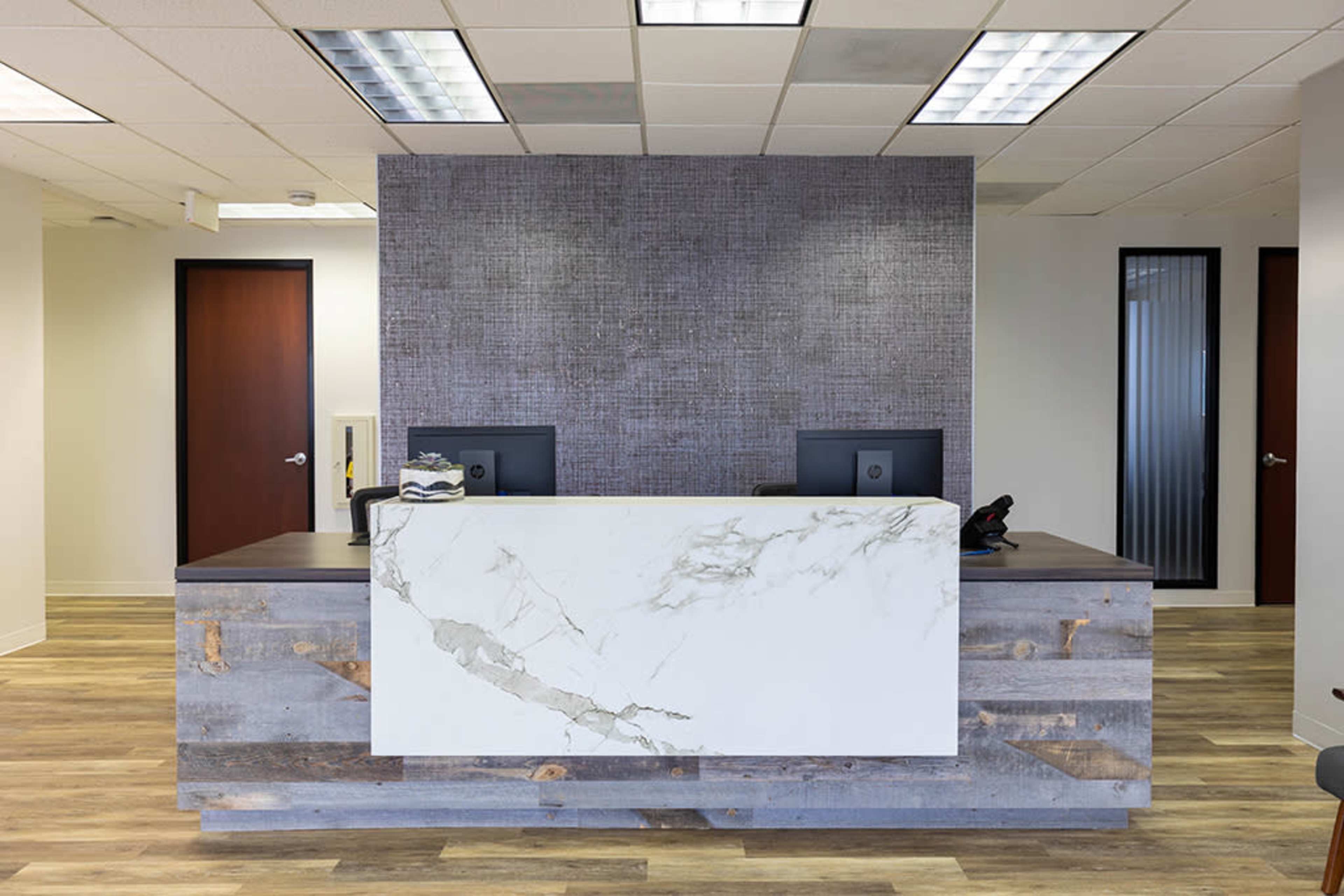 A modern reception area with a marble-topped desk and computer monitors set against a textured gray wall.