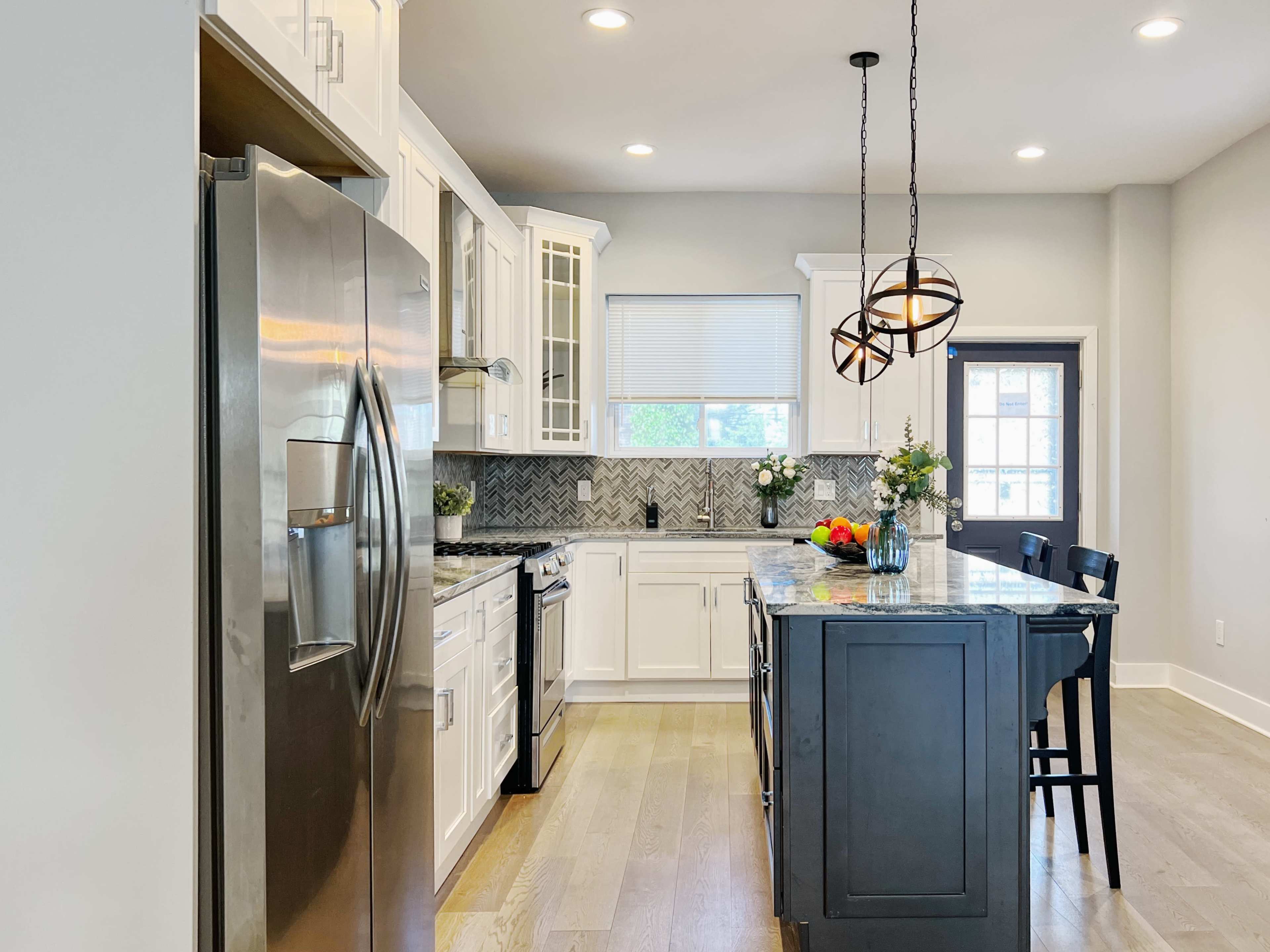 A modern kitchen with white cabinets, a dark island, and stainless steel appliances.