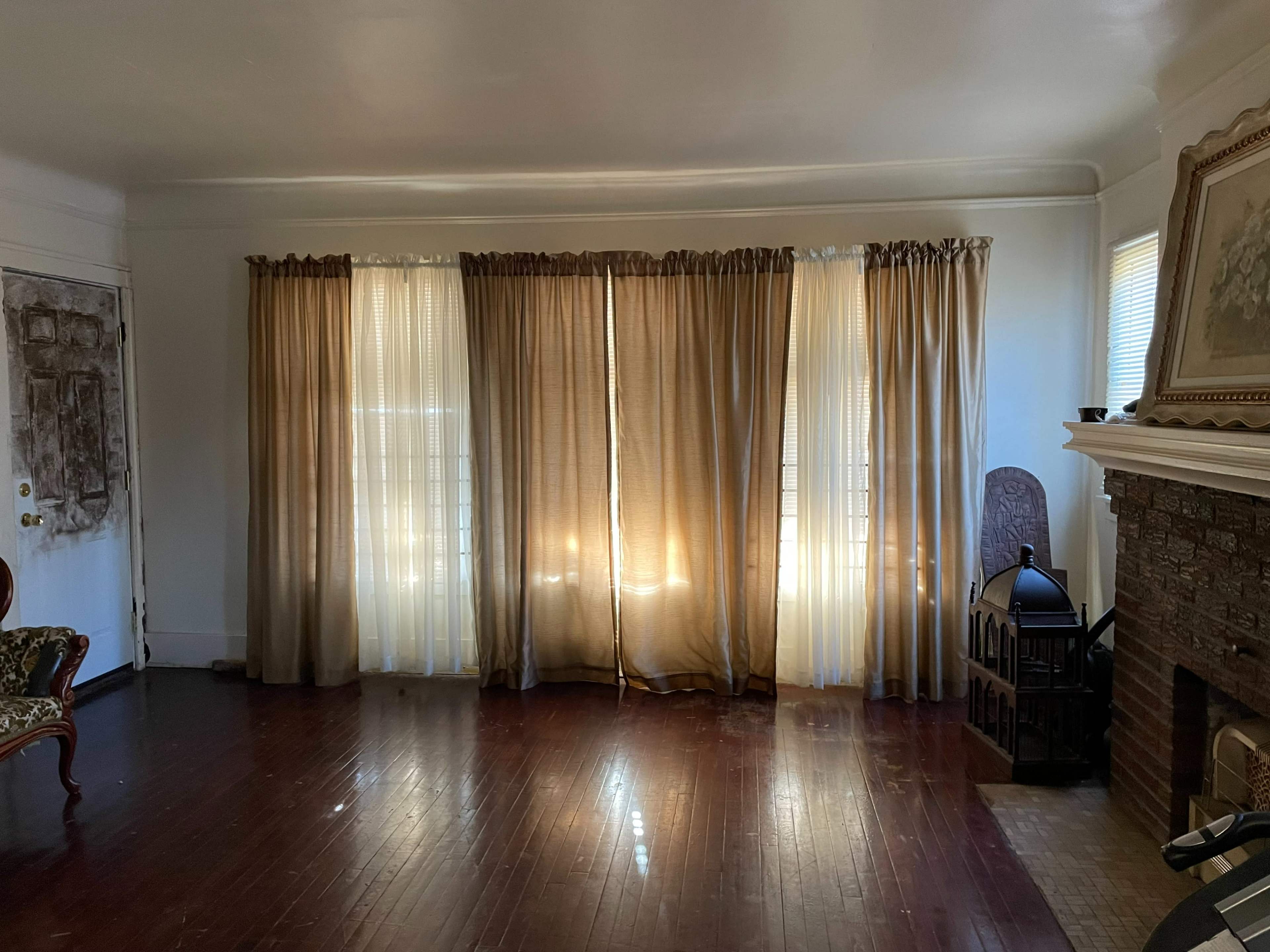 The room features a set of floor-length curtains covering windows, casting light onto a hardwood floor in front of a stone fireplace.