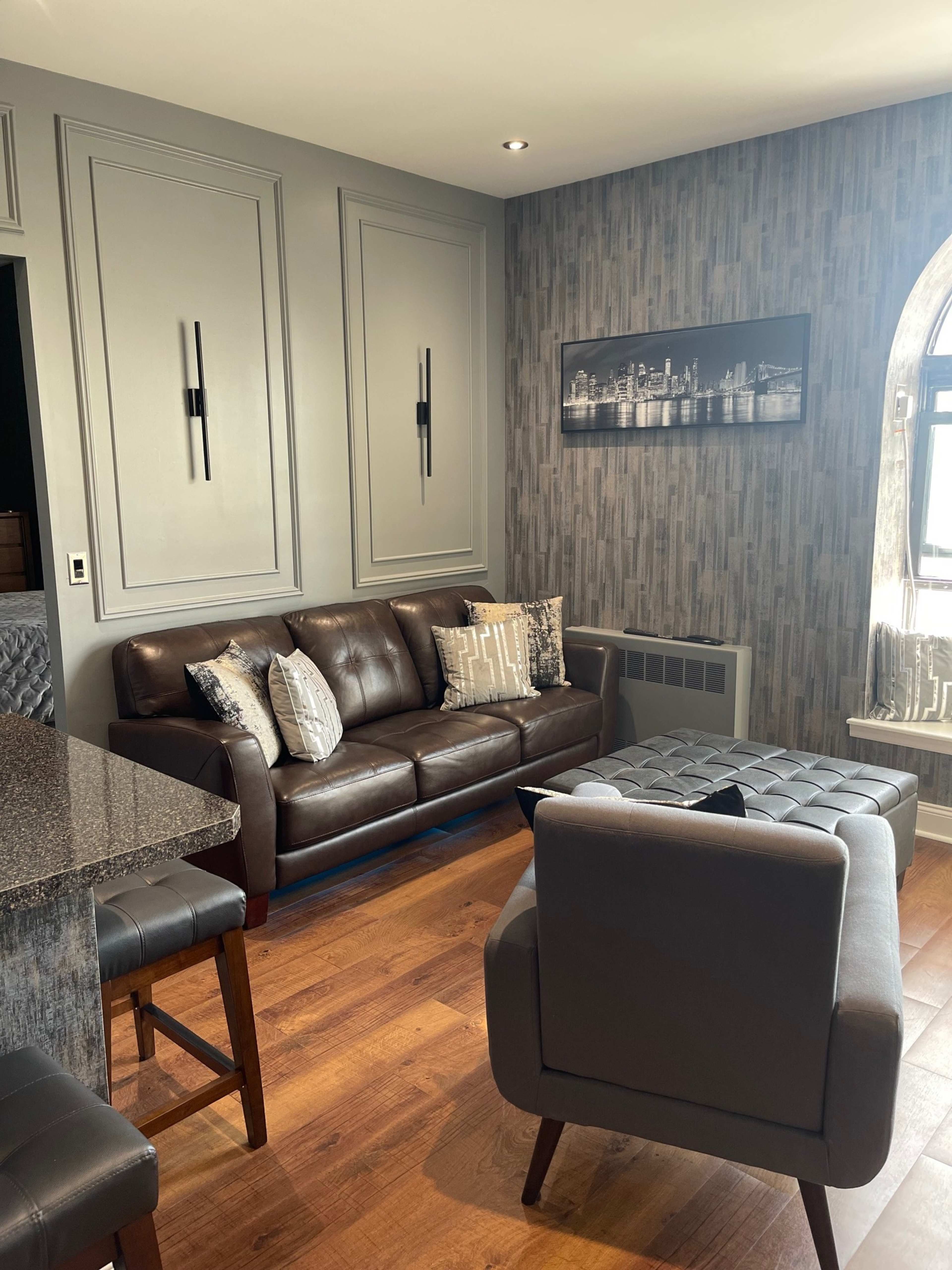 A modern living room featuring a dark leather sofa with decorative pillows, a coffee table, and patterned wallpaper.