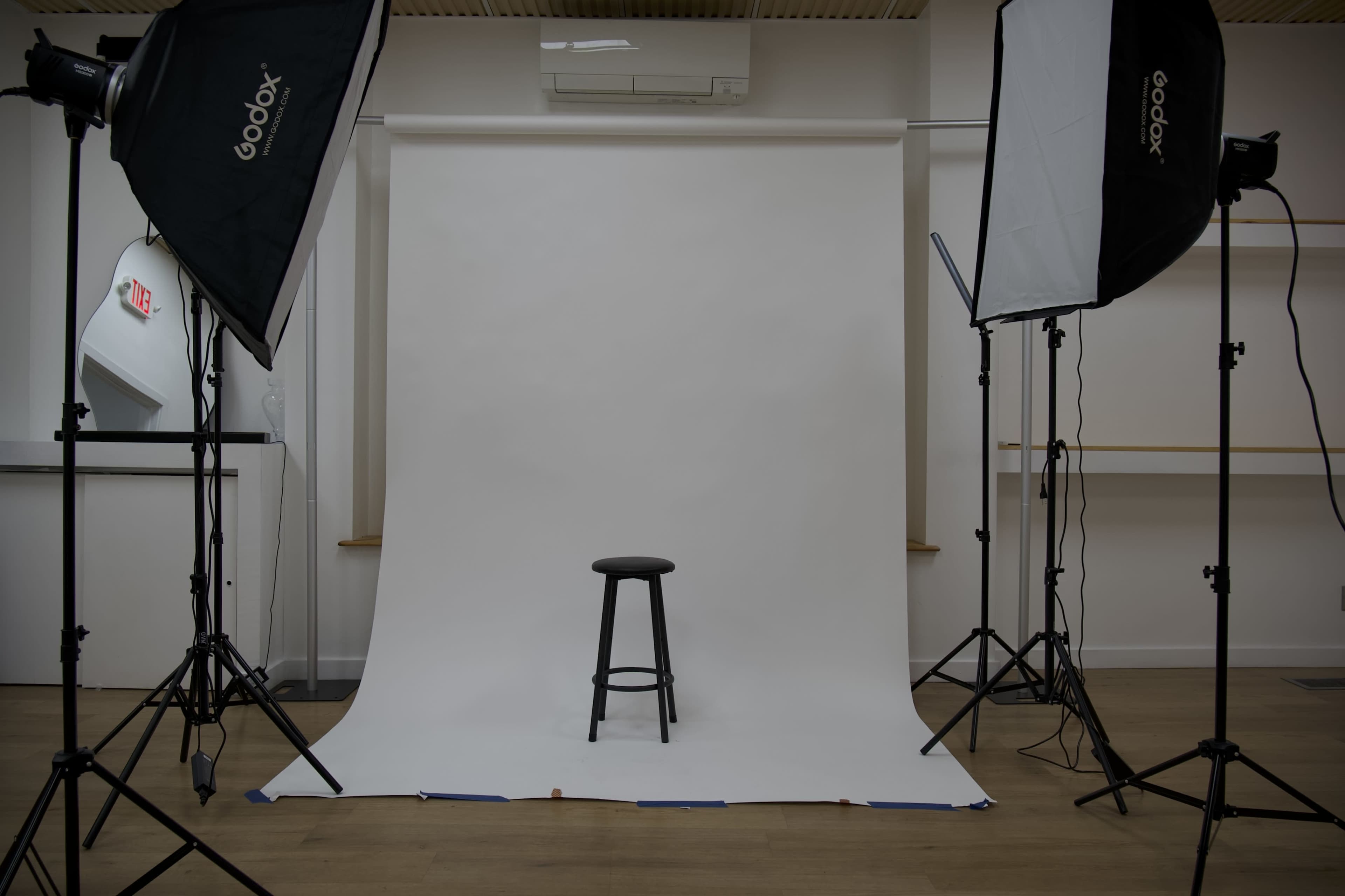 A black stool is positioned on a white backdrop, surrounded by studio lighting equipment.