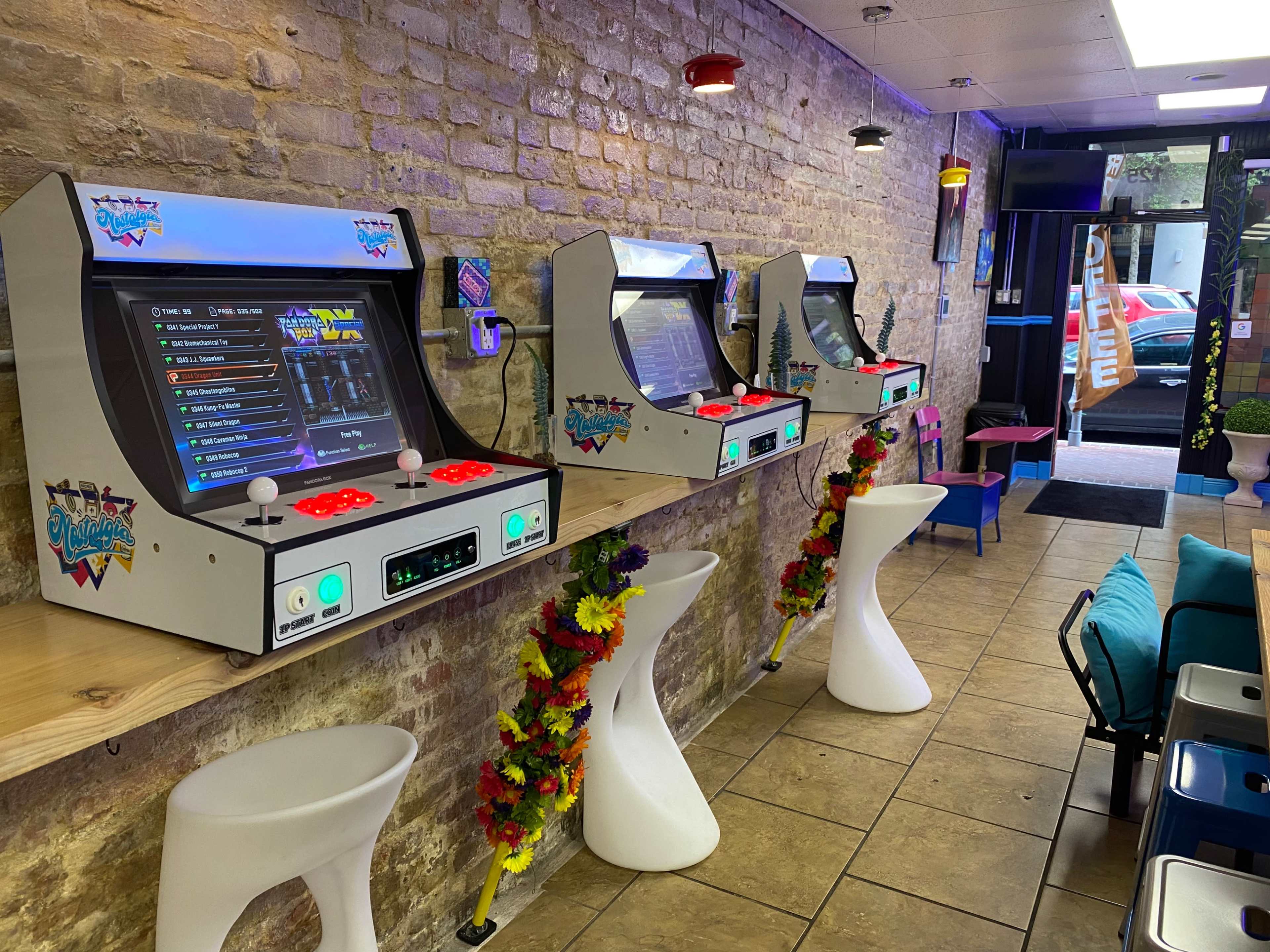 A row of three modern arcade machines lined against a brick wall in a brightly lit gaming center.
