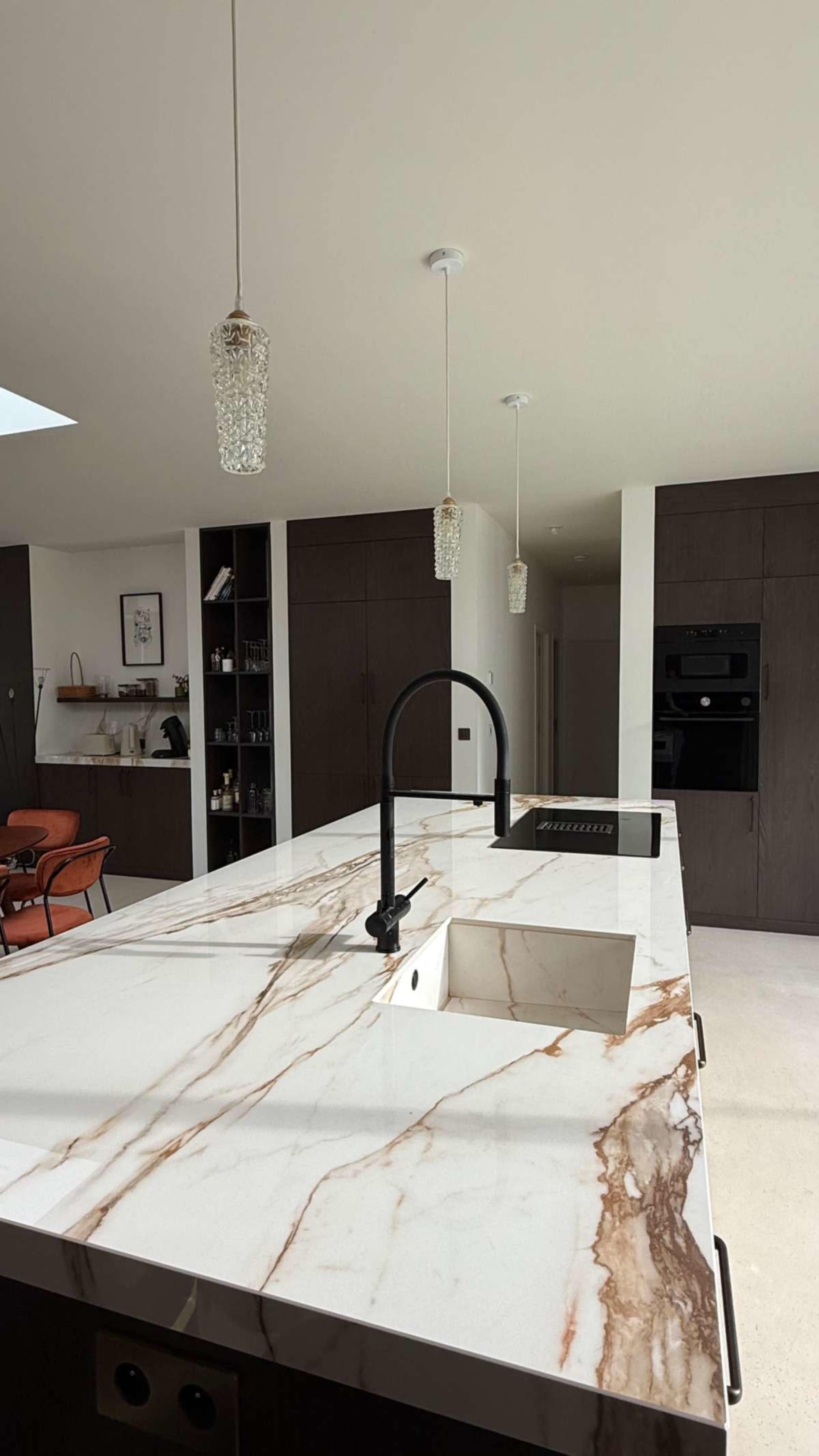 The image shows a modern kitchen featuring a marble countertop with veins of color, a sleek black faucet, pendant lighting, and cabinetry.