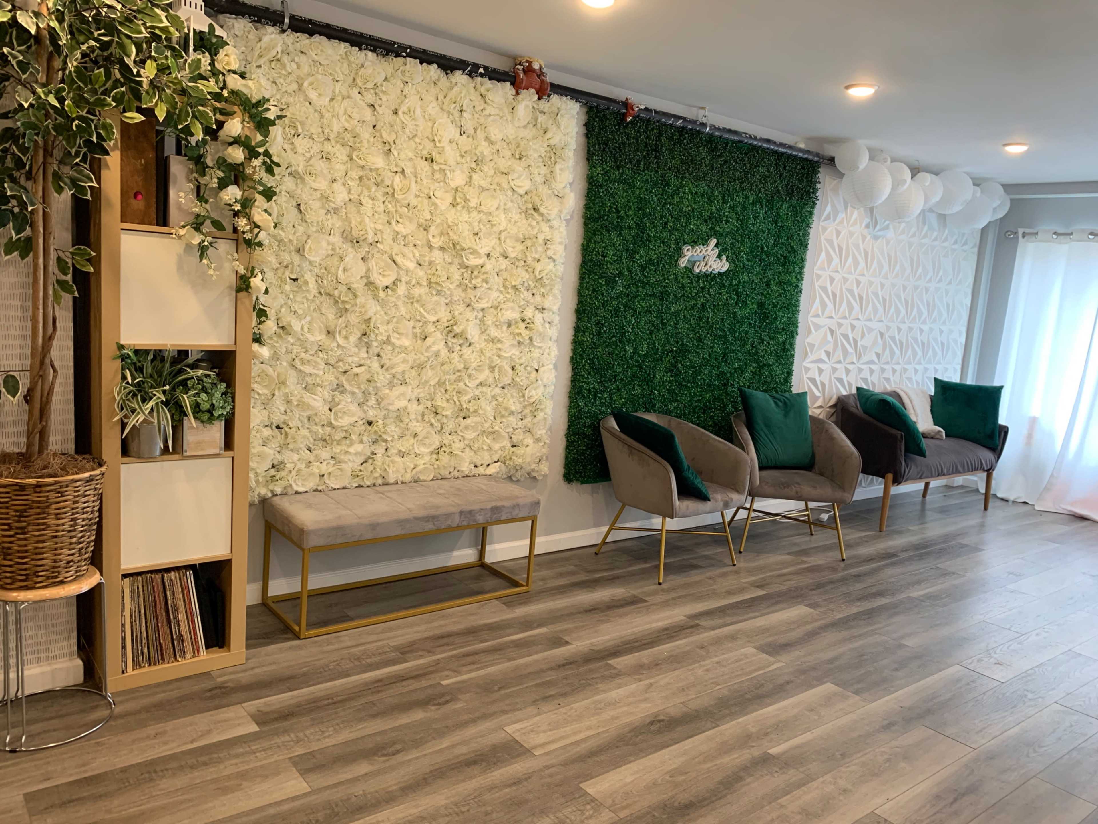 A spacious room features a flower wall, a green moss wall, two modern chairs, a bench, and decorative elements, all set on a wooden floor.