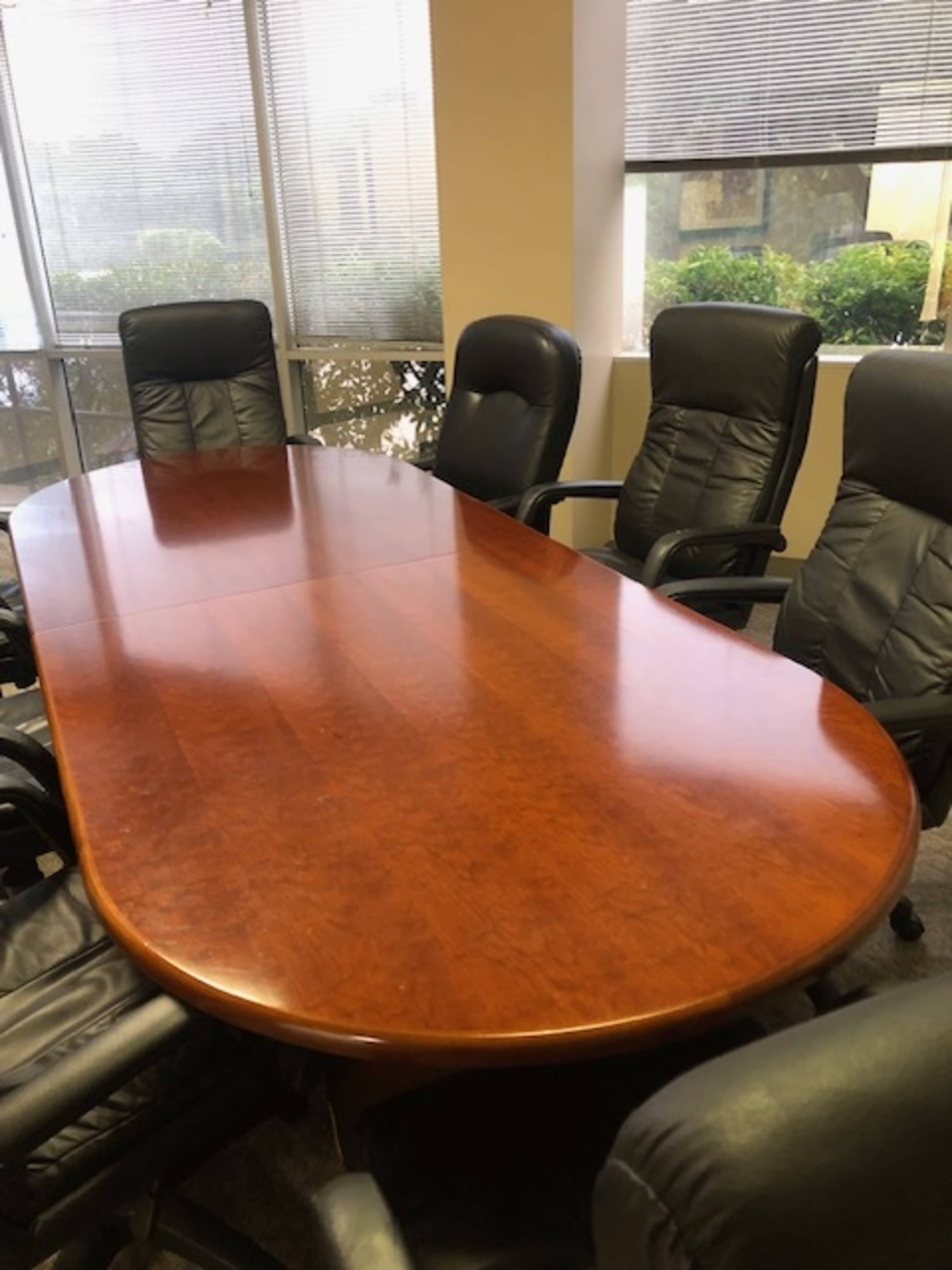 A large wooden conference table is surrounded by six black leather office chairs in a well-lit meeting room.