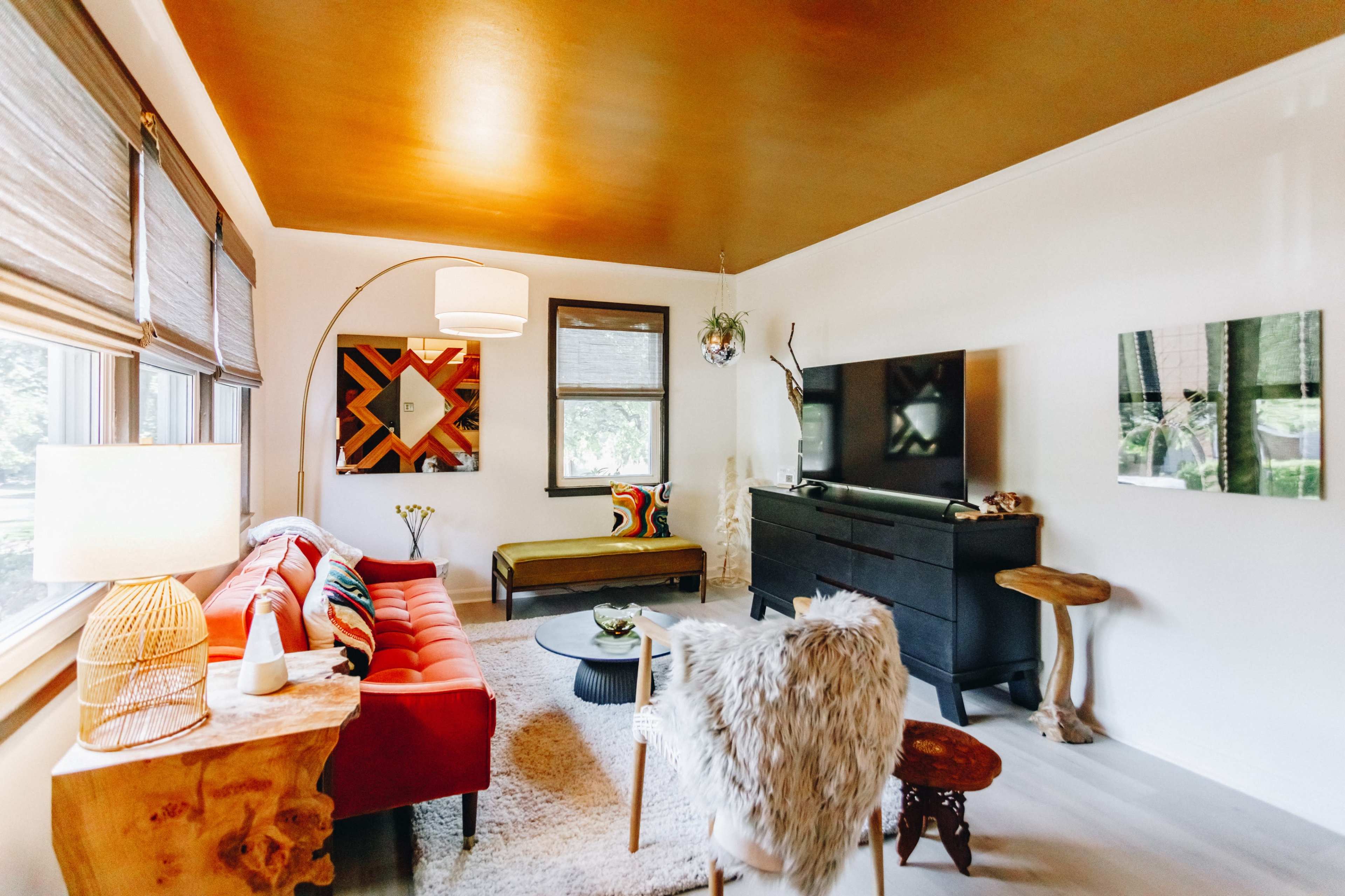The living room features a red sofa, a dark console table with a television, and various decorative elements against a golden ceiling and light-colored walls.