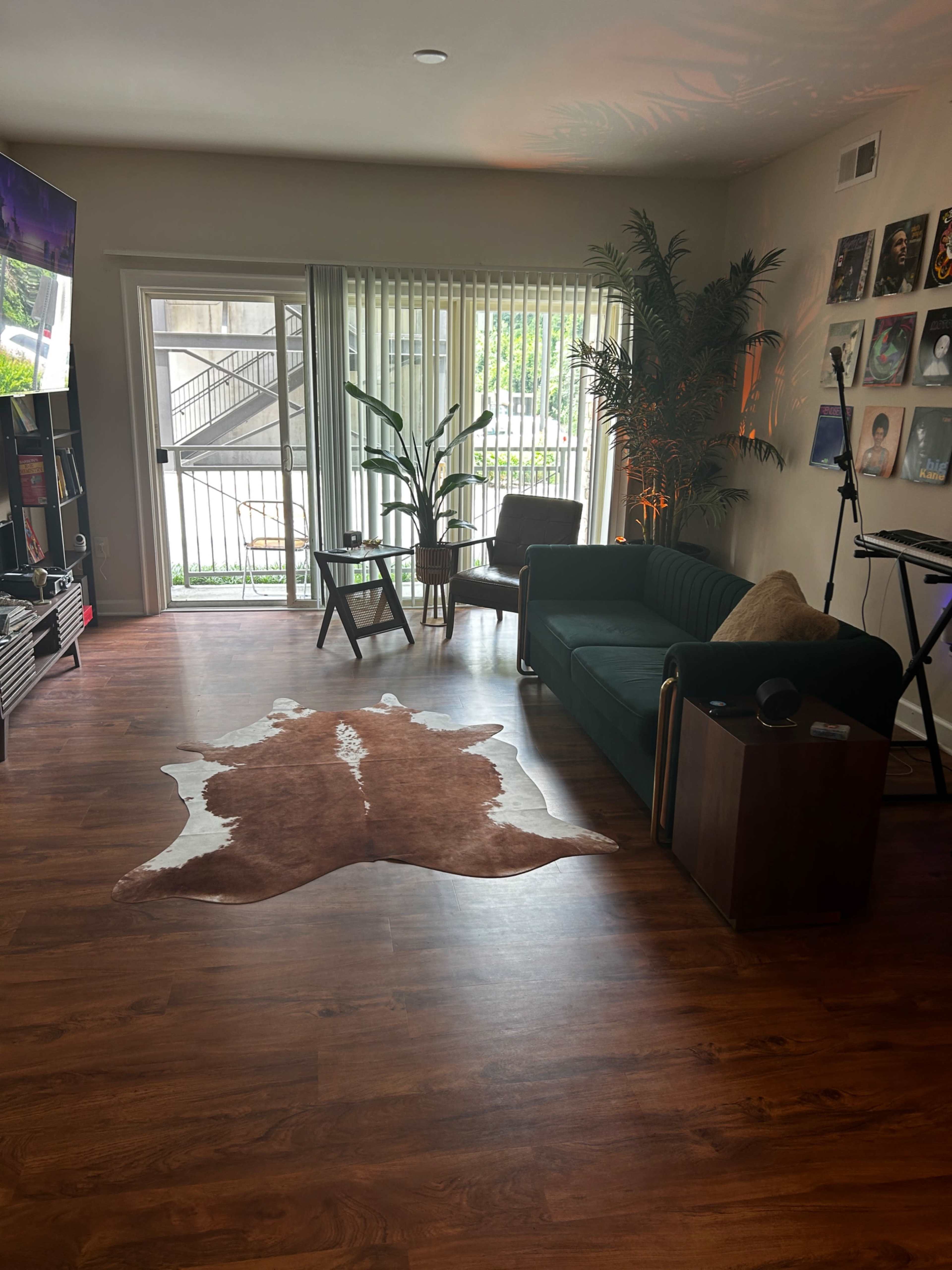The living room features a dark green couch, a wooden chair, and a rug on the floor, with sliding glass doors leading to an outdoor area.