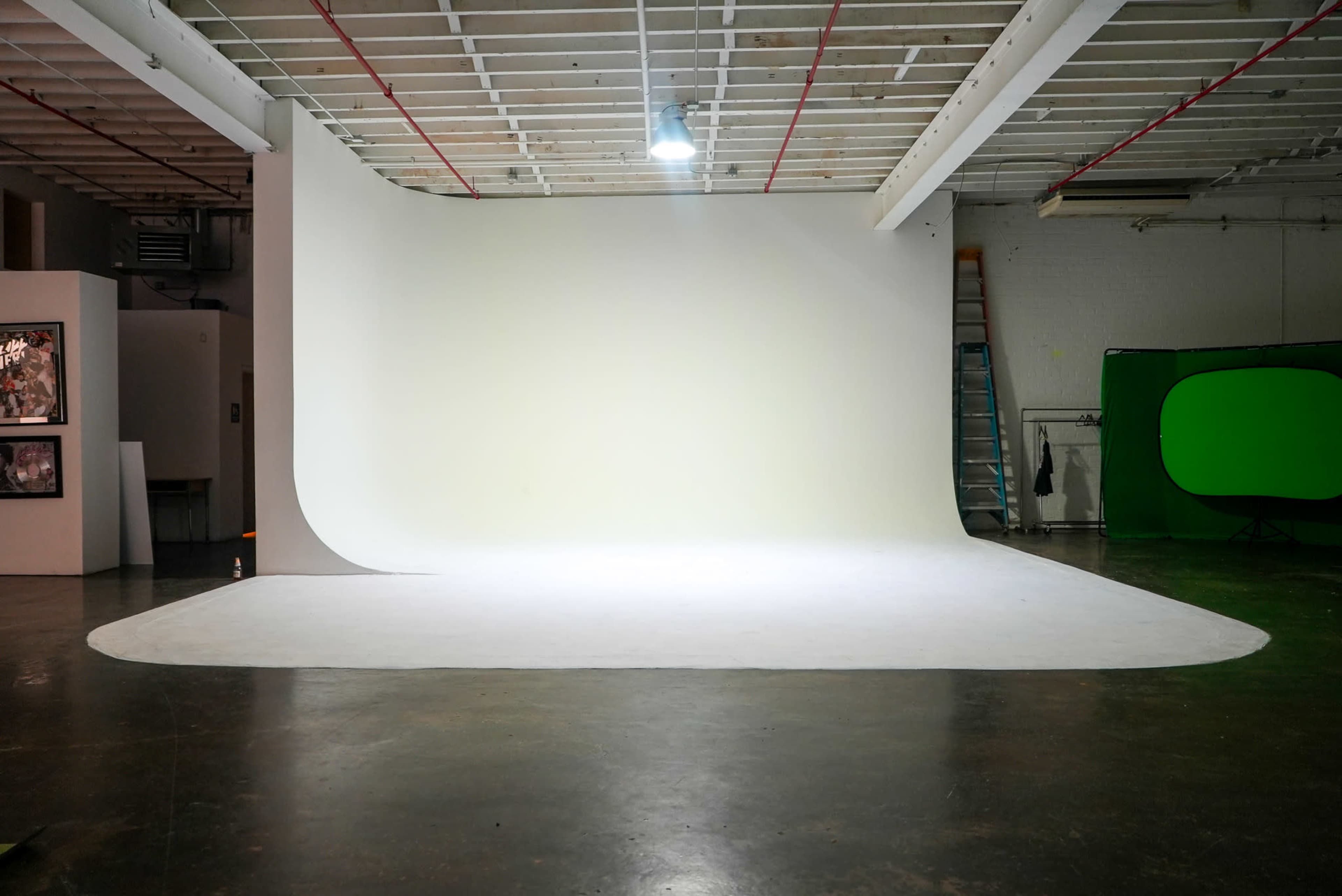 The image shows a spacious photography studio with a seamless white backdrop and a green screen setup in the corner.