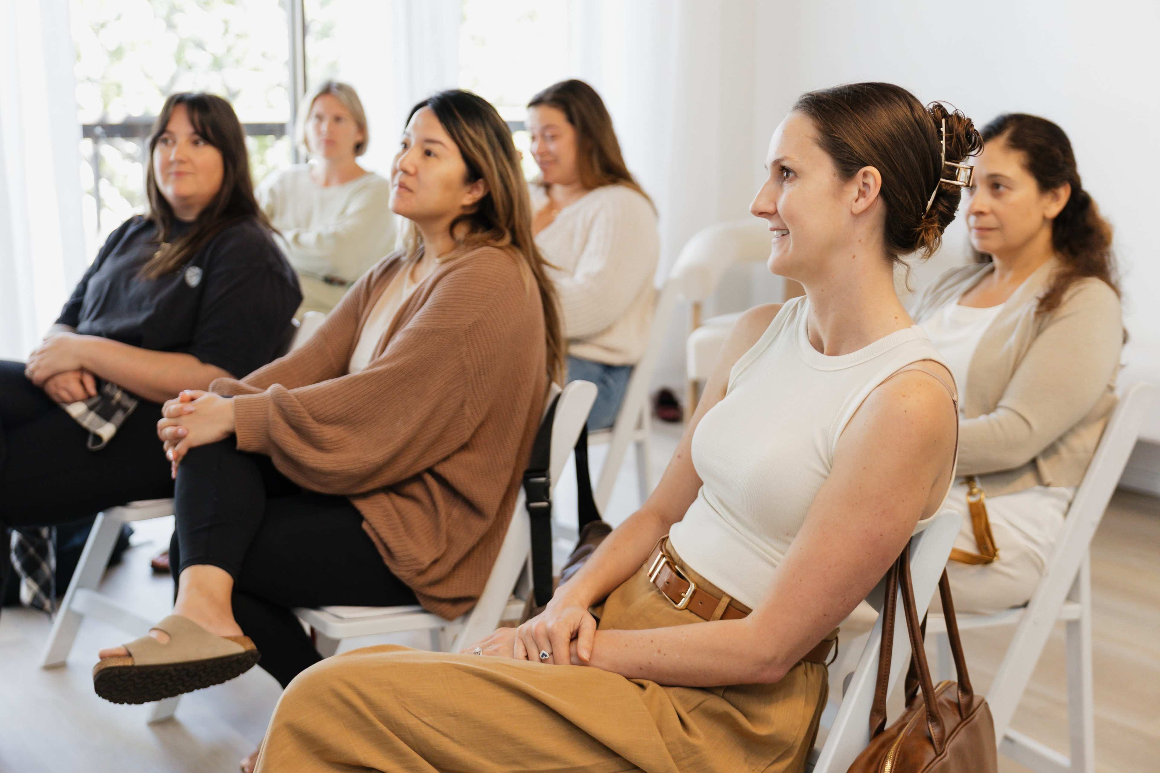 A group of five women sits attentively in a well-lit room, engaged in a discussion.
