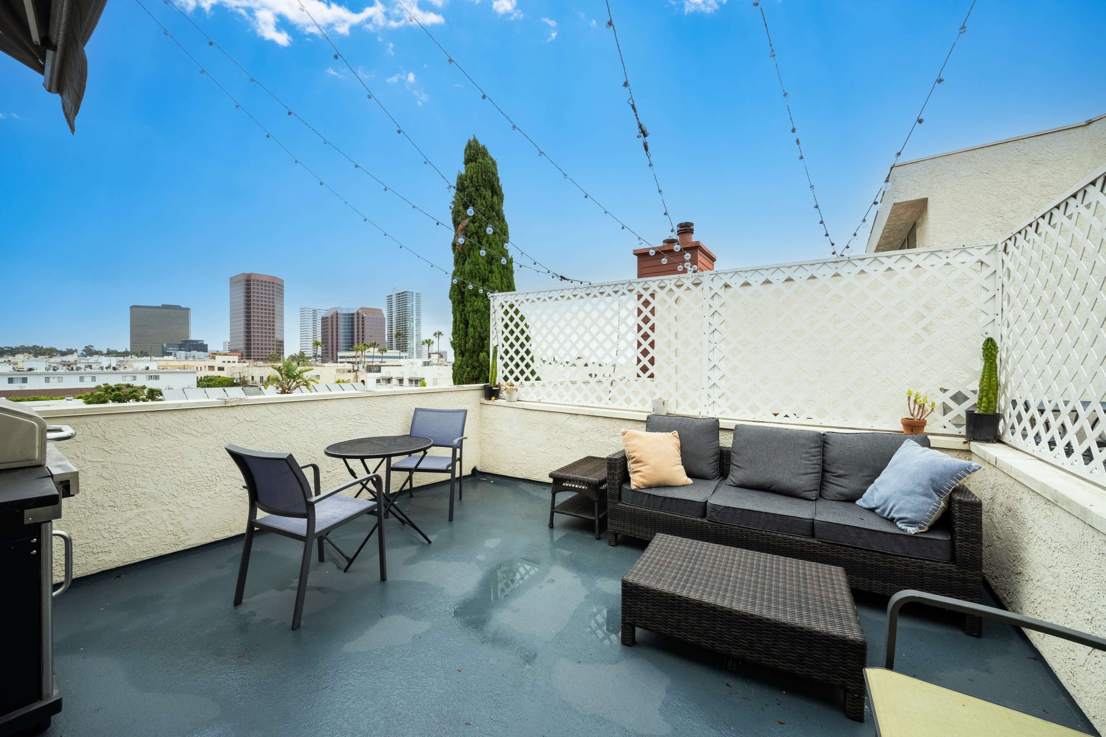 A rooftop patio with a seating area, a small table, and a view of city buildings in the background.