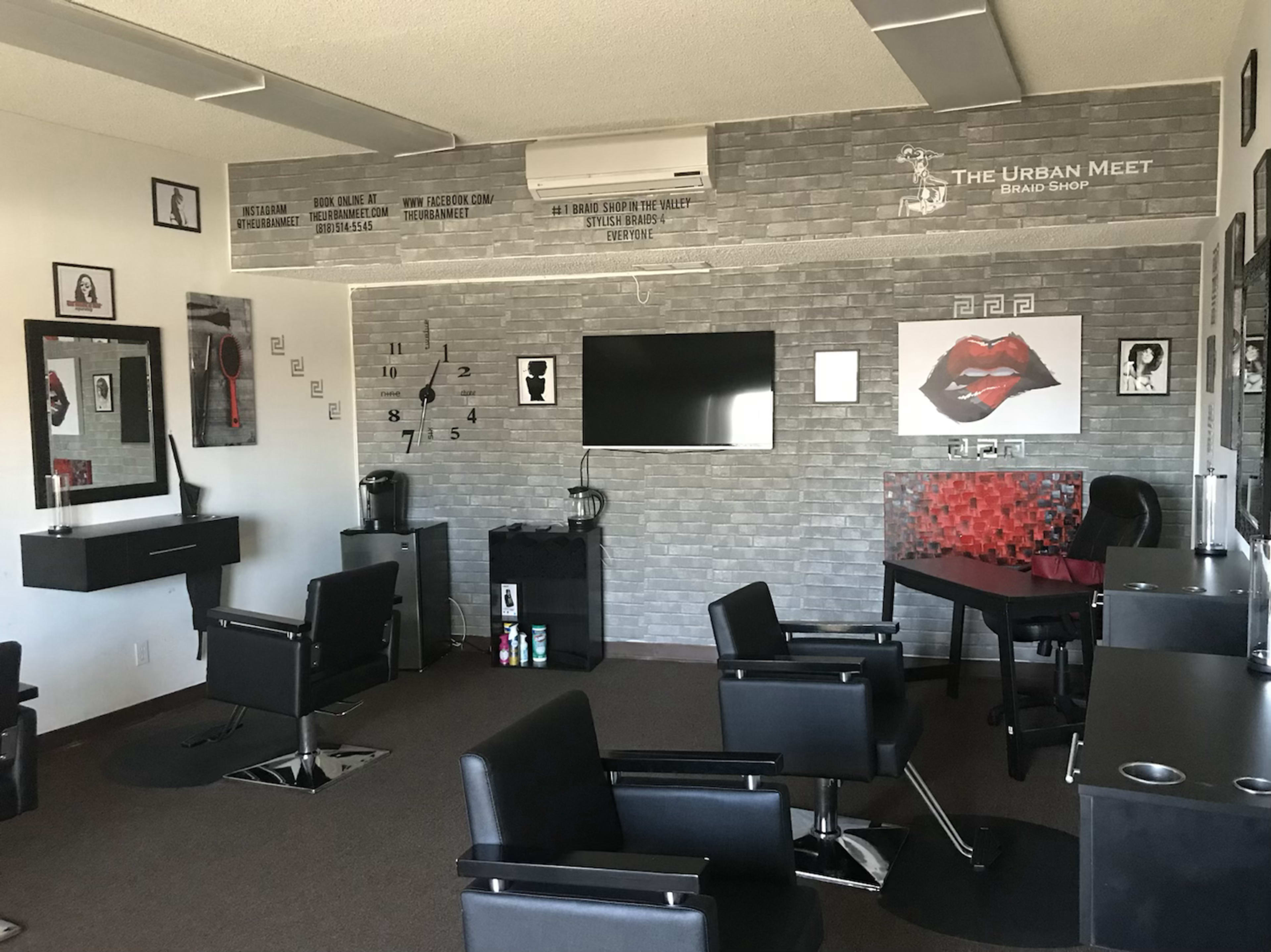 A modern barbershop interior with black chairs, a wall-mounted television, and decor featuring mirrors and artwork.