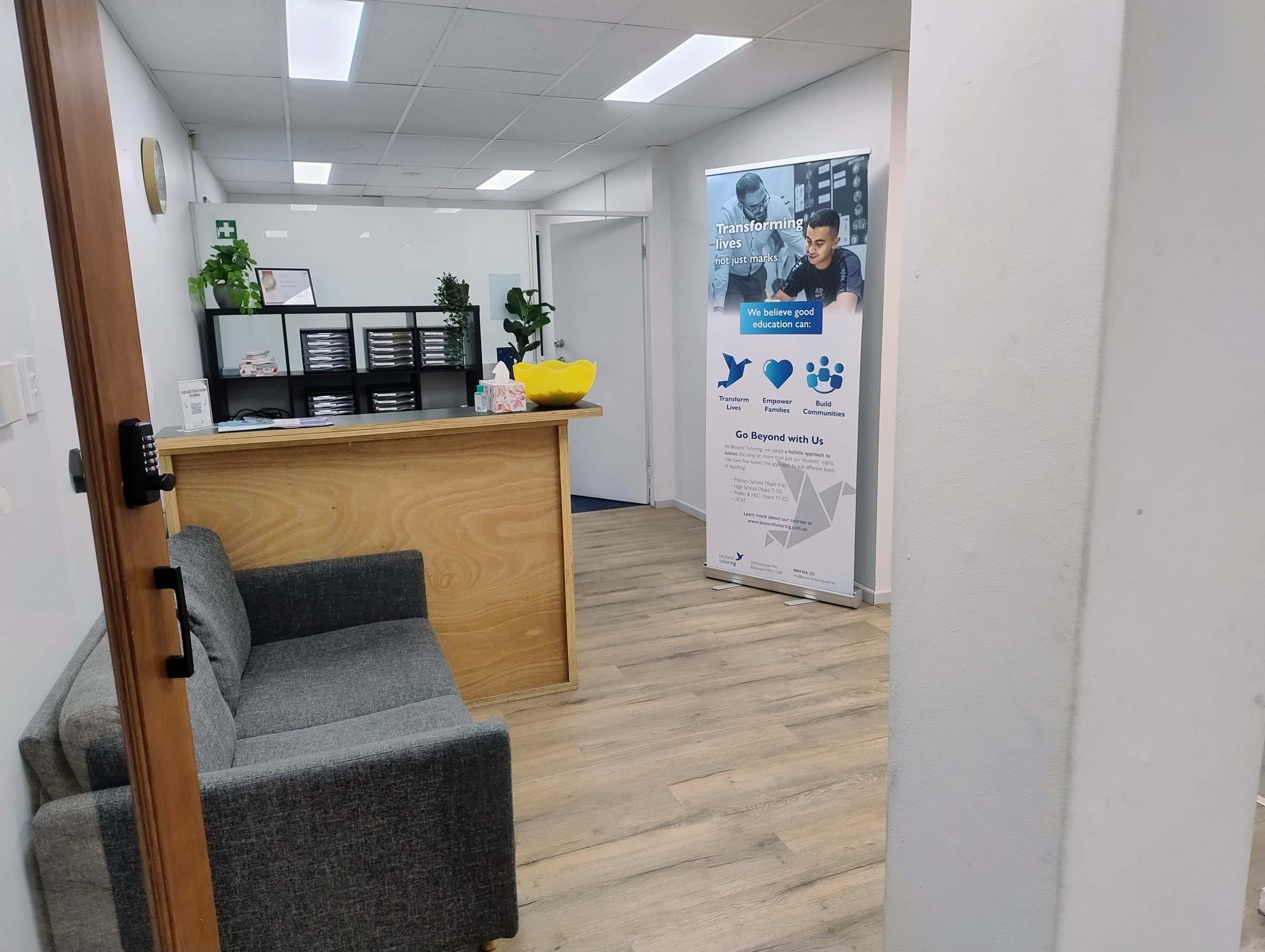 The image shows a reception area with a wooden front desk, a gray sofa, and a banner promoting services on the wall.