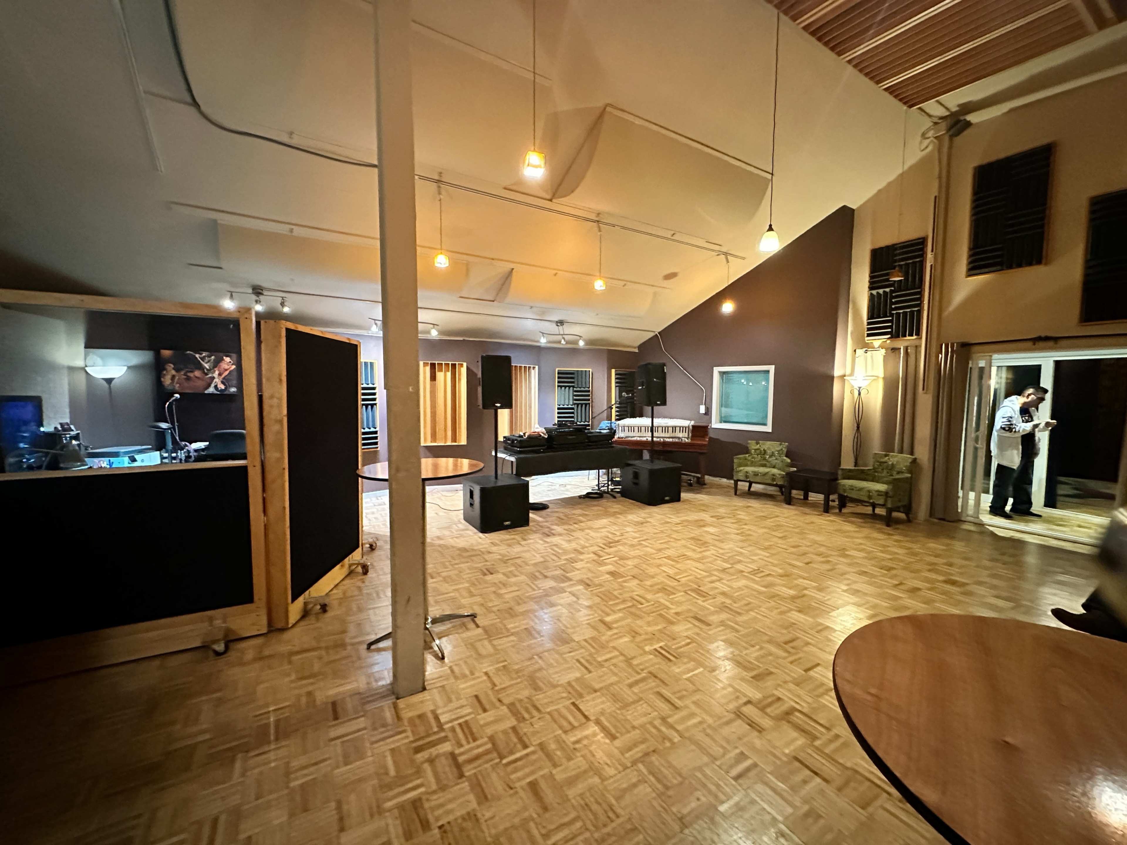A spacious recording studio with wooden flooring, an area for sound equipment, and two green chairs near the entrance.