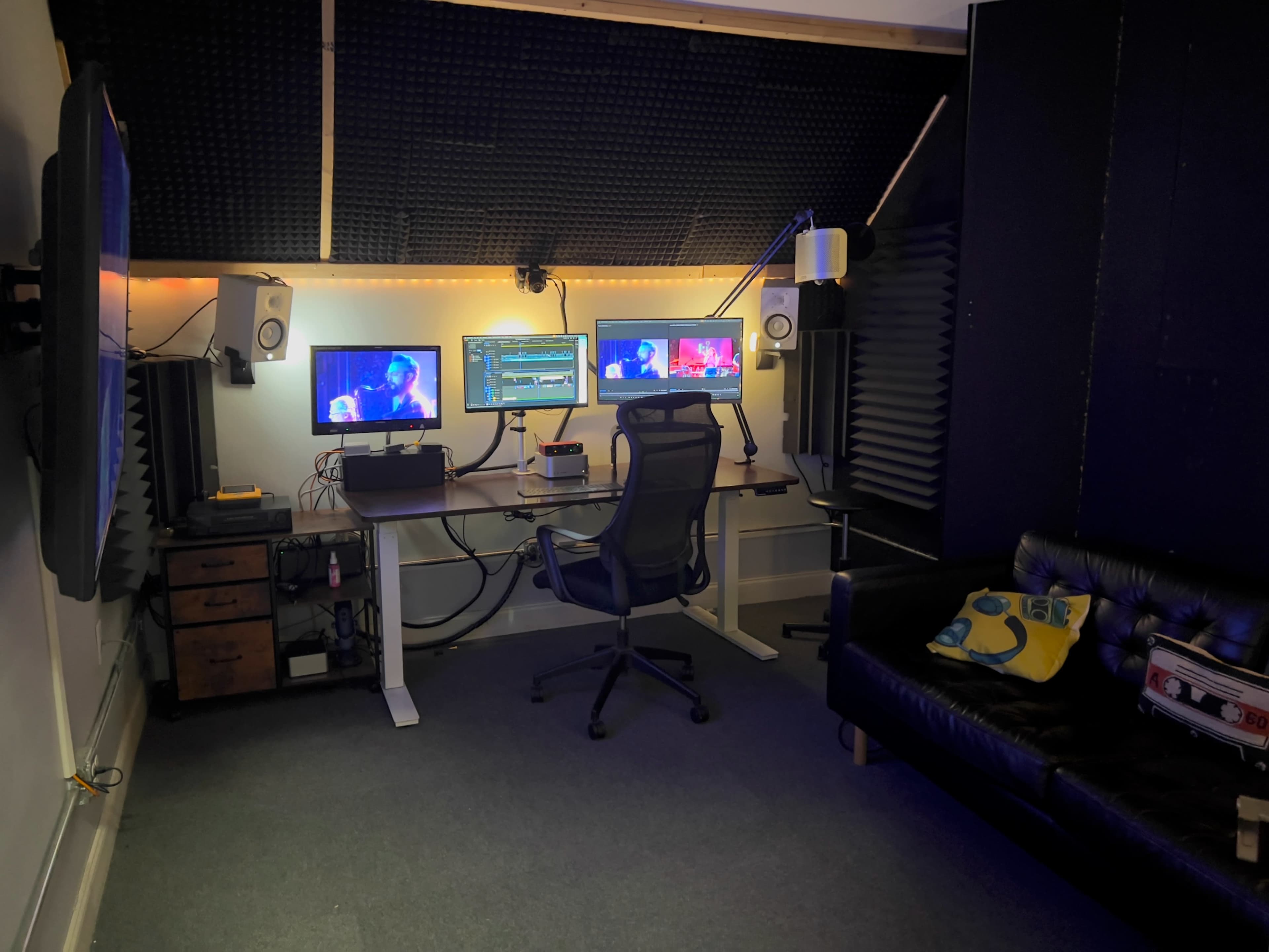 The image shows a modern workspace with two computer monitors, a desk with an office chair, and a black sofa in a soundproofed room.