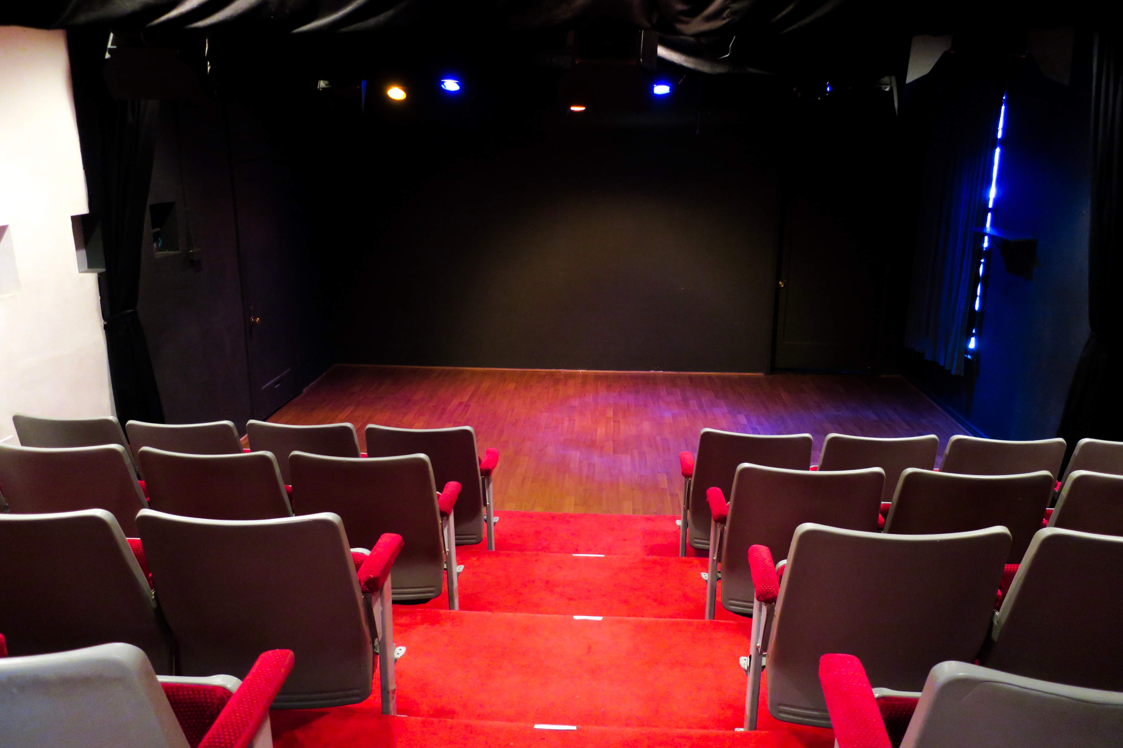 A small theater with red carpeted seating and a dark stage illuminated by overhead lights.
