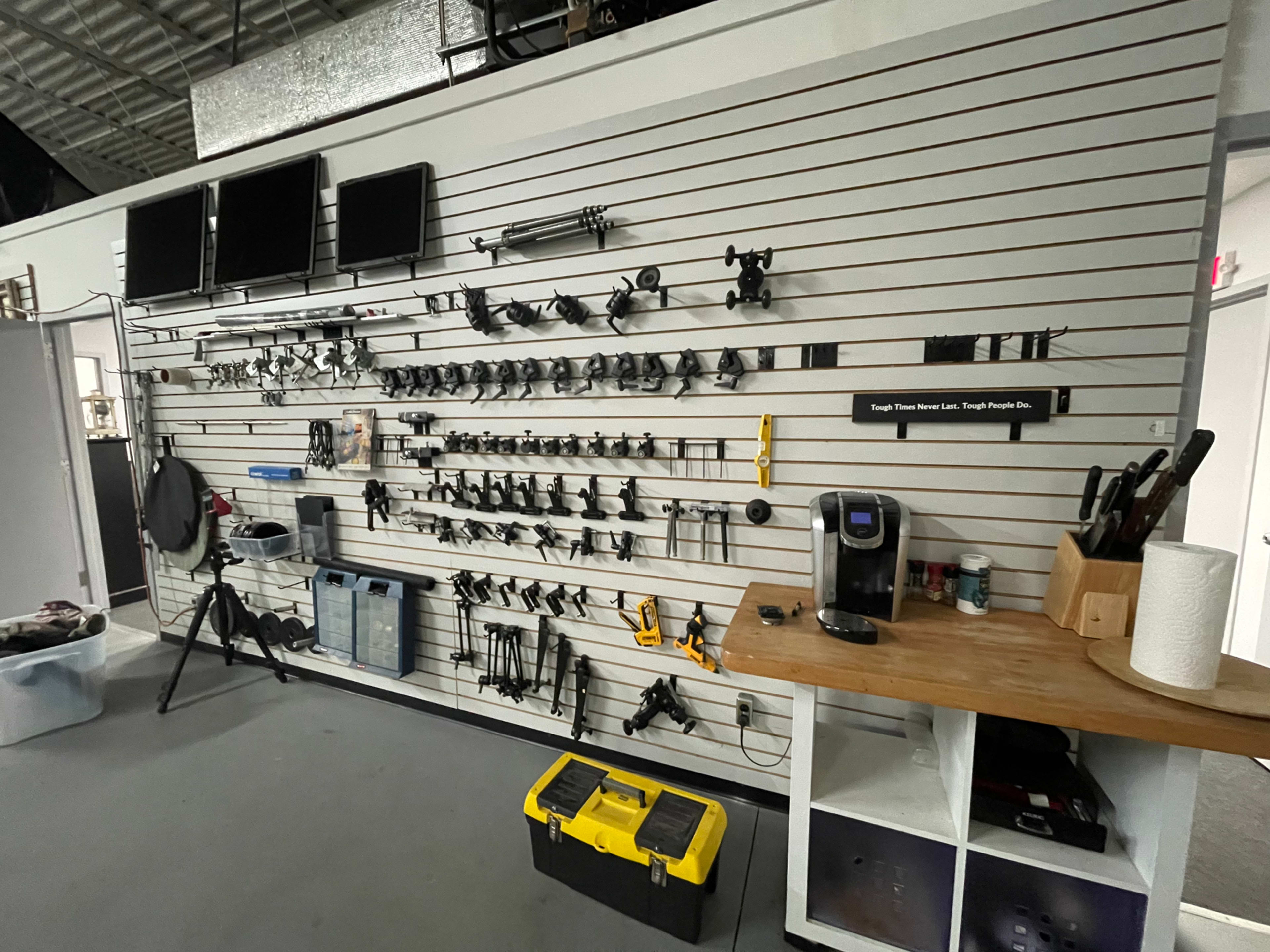 A wall with various tools and equipment organized on hooks, alongside a wooden workbench with a coffee maker and storage containers.