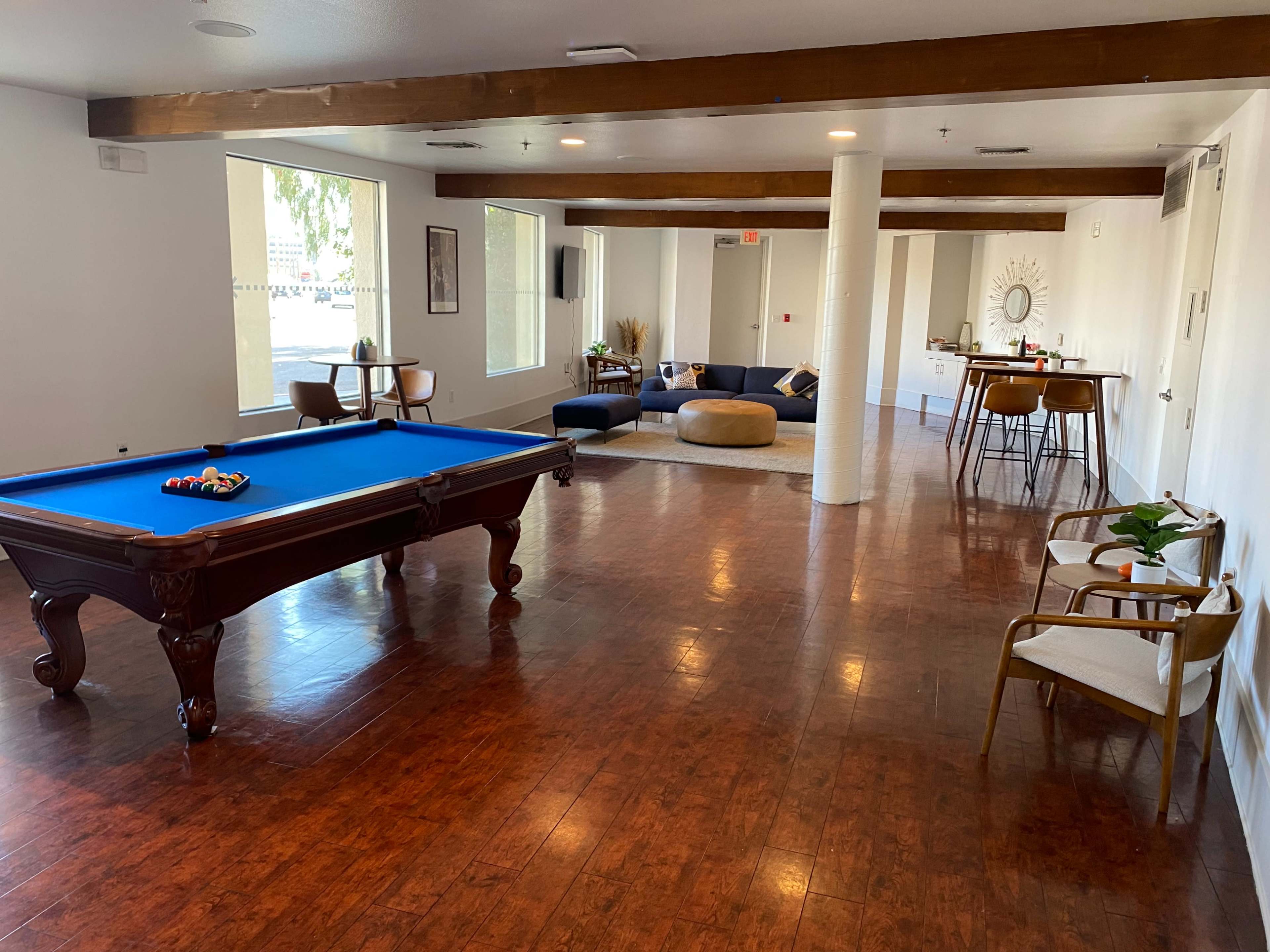 The image shows an interior recreational space featuring a billiard table with a blue felt surface, along with a seating area that includes a sofa, chairs, and a small dining table.