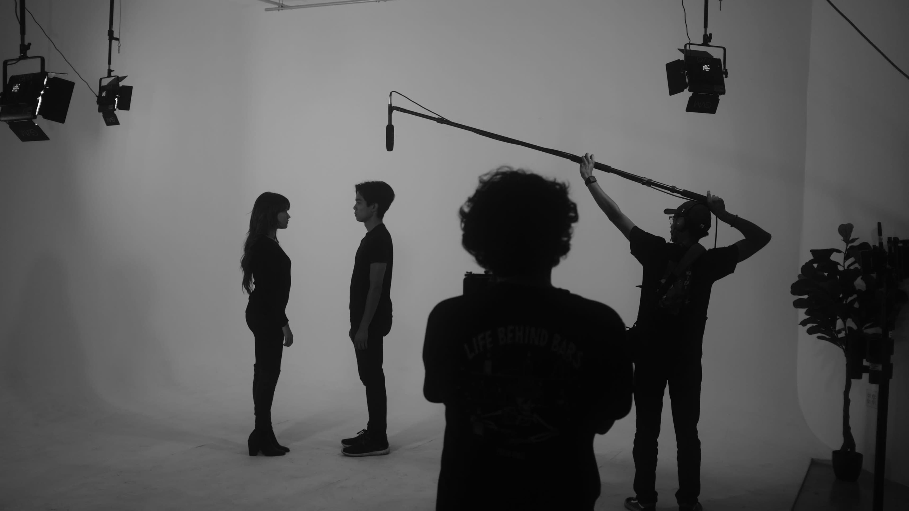 Two individuals stand facing each other in a studio setting, while a crew member holds a microphone on a boom.