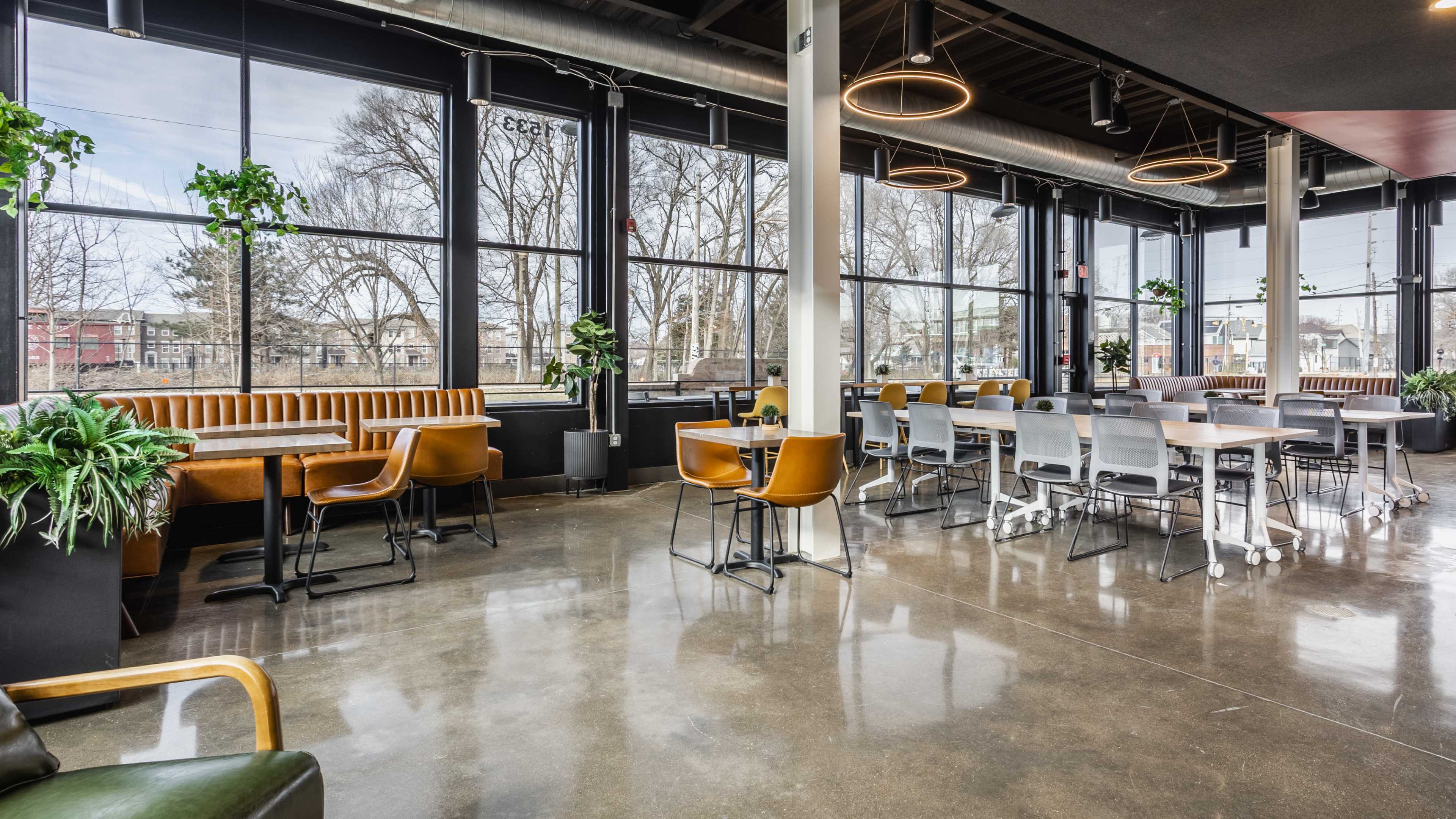 The image features a modern café interior with large windows, a mix of seating options, and polished concrete floors.