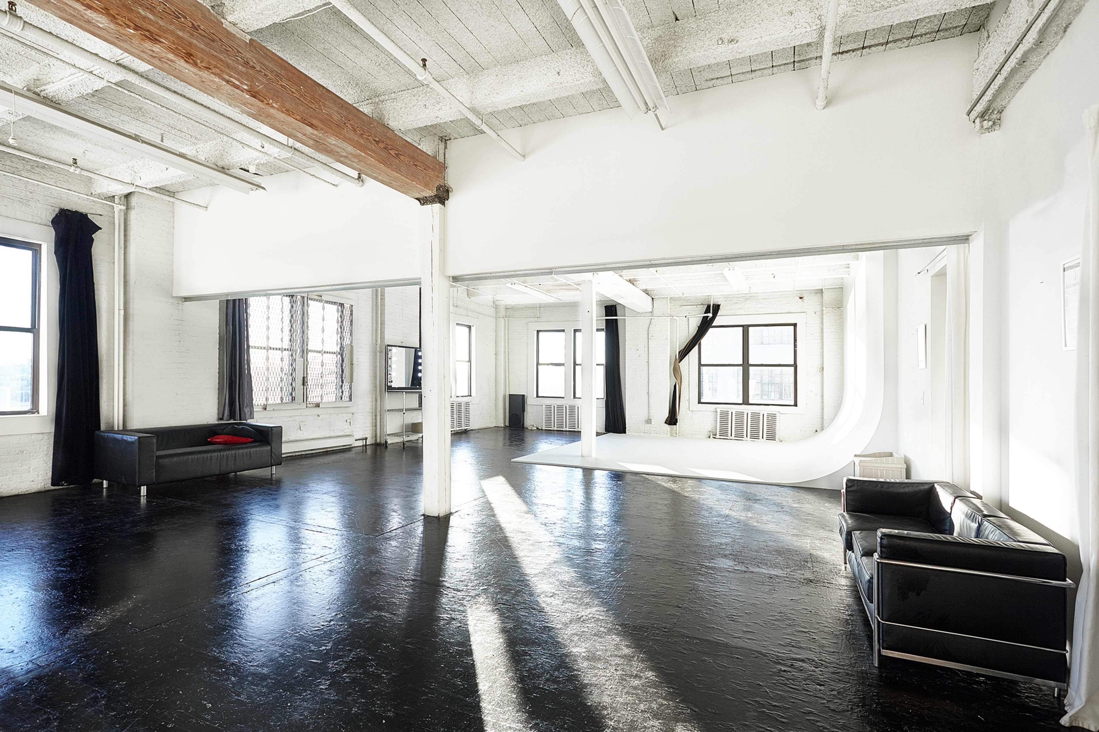 A spacious, modern studio with large windows, polished black floors, and minimal furniture.