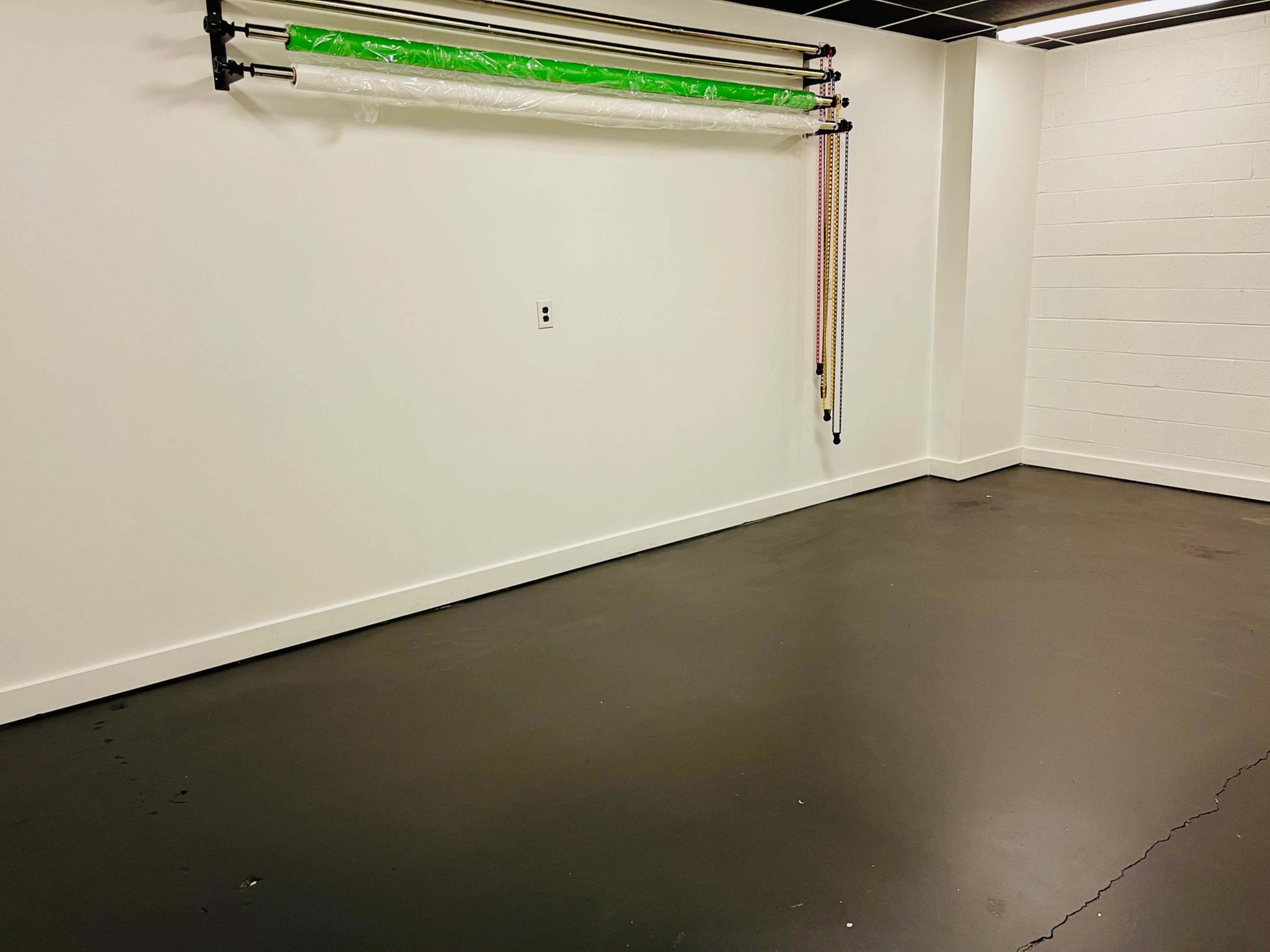 An empty room with a smooth dark floor and a green backdrop roll mounted on the wall.