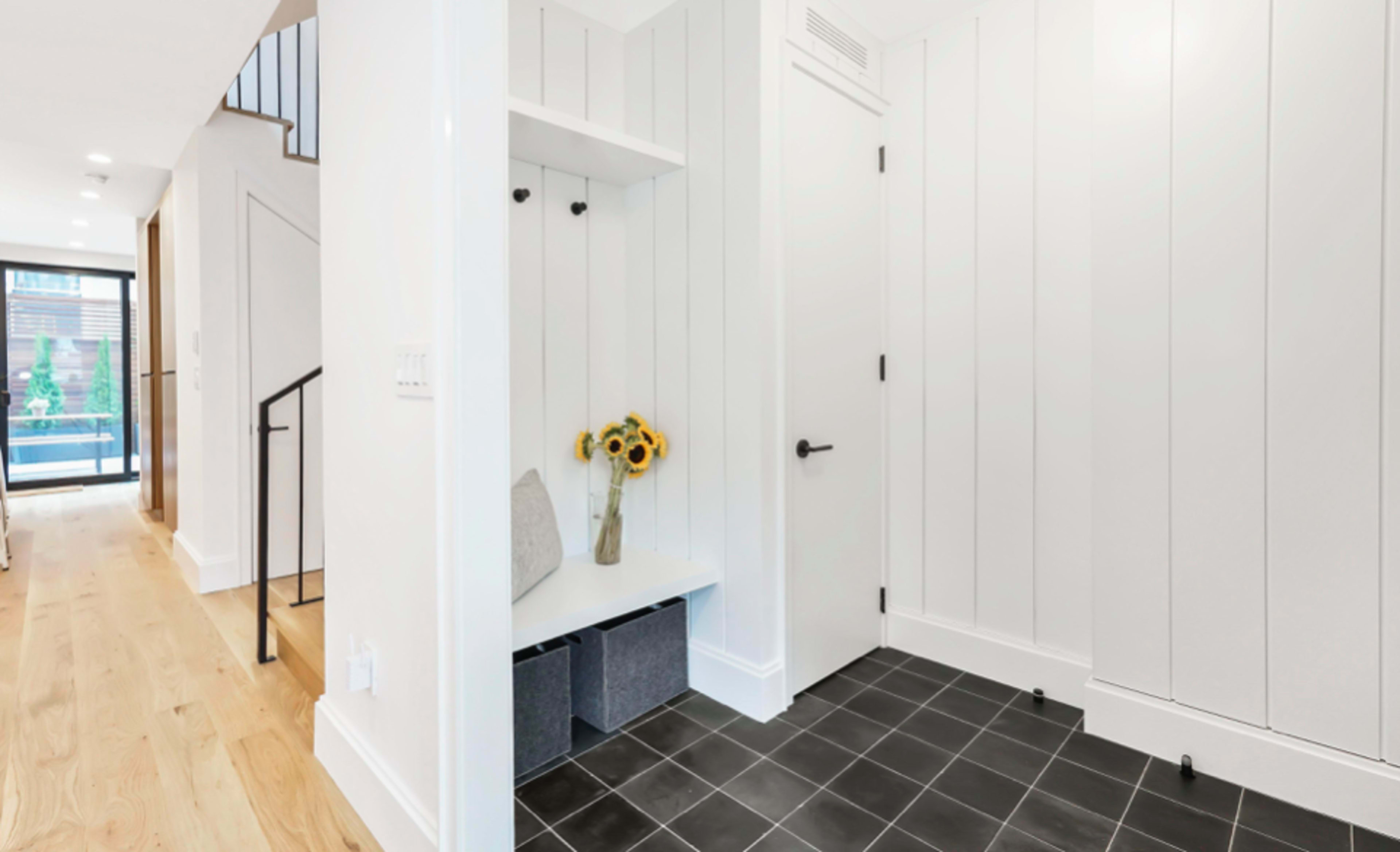 A modern entryway with white shiplap walls, a small bench with sunflowers, and black tiled flooring.