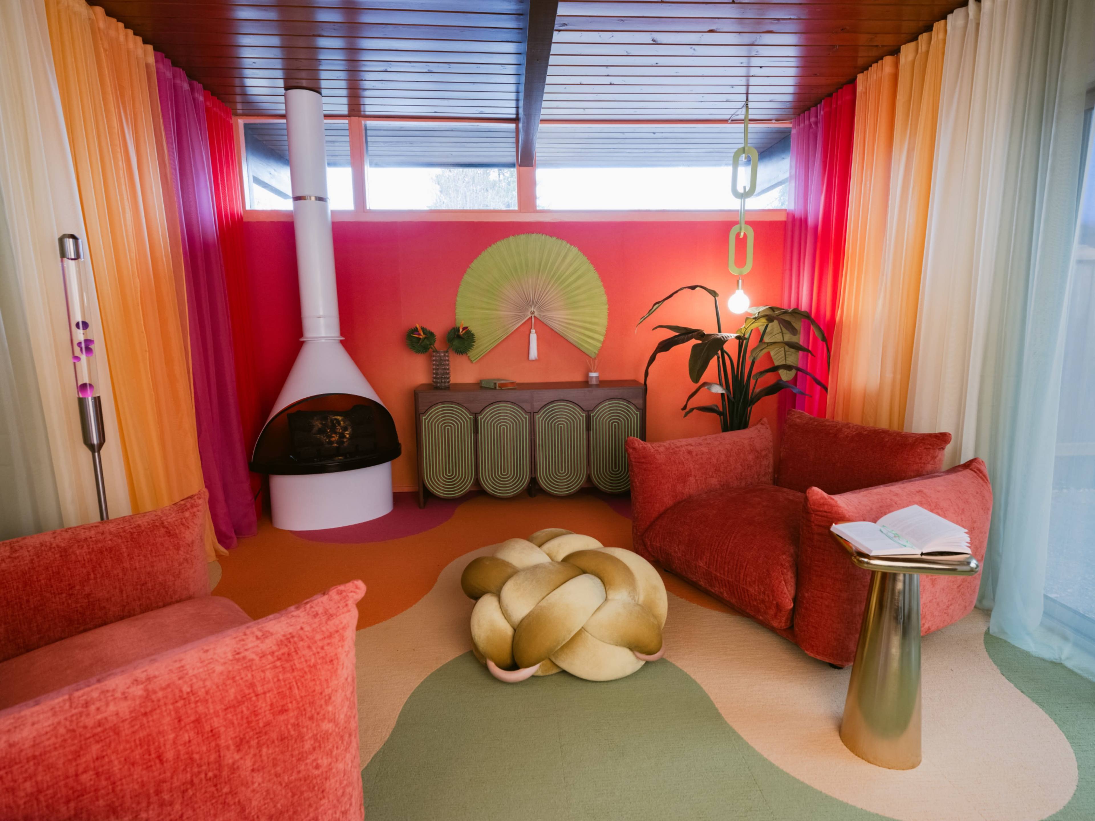 The image features a vibrant living room with colorful curtains, a modern fireplace, and distinctive furniture, including two plush sofas and a unique coffee table.