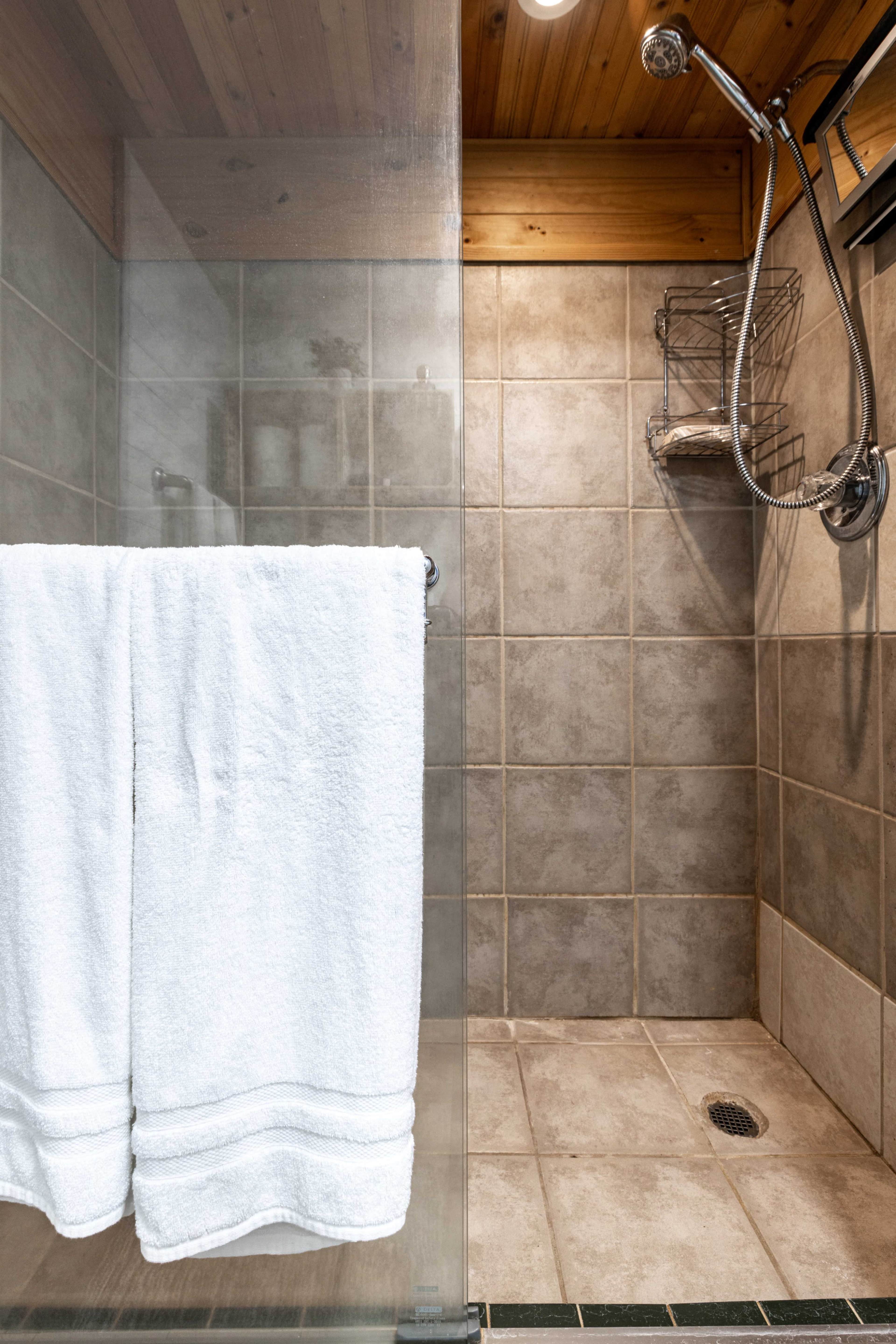 The image shows a glass shower enclosure with beige tiled walls and a hanging white towel on a chrome rack.