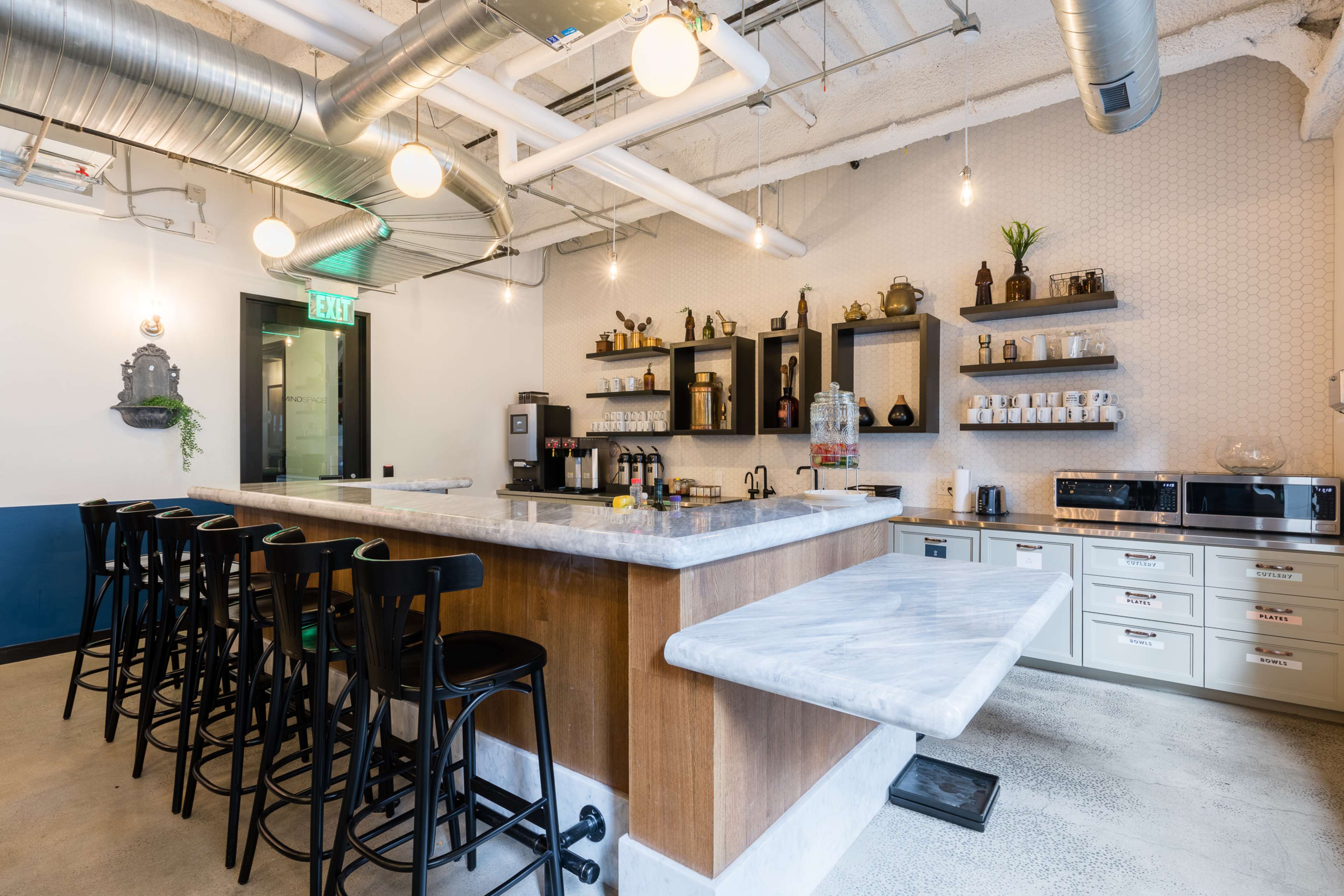 A modern kitchen with a marble countertop island, black bar stools, and shelves displaying various kitchen items and appliances.