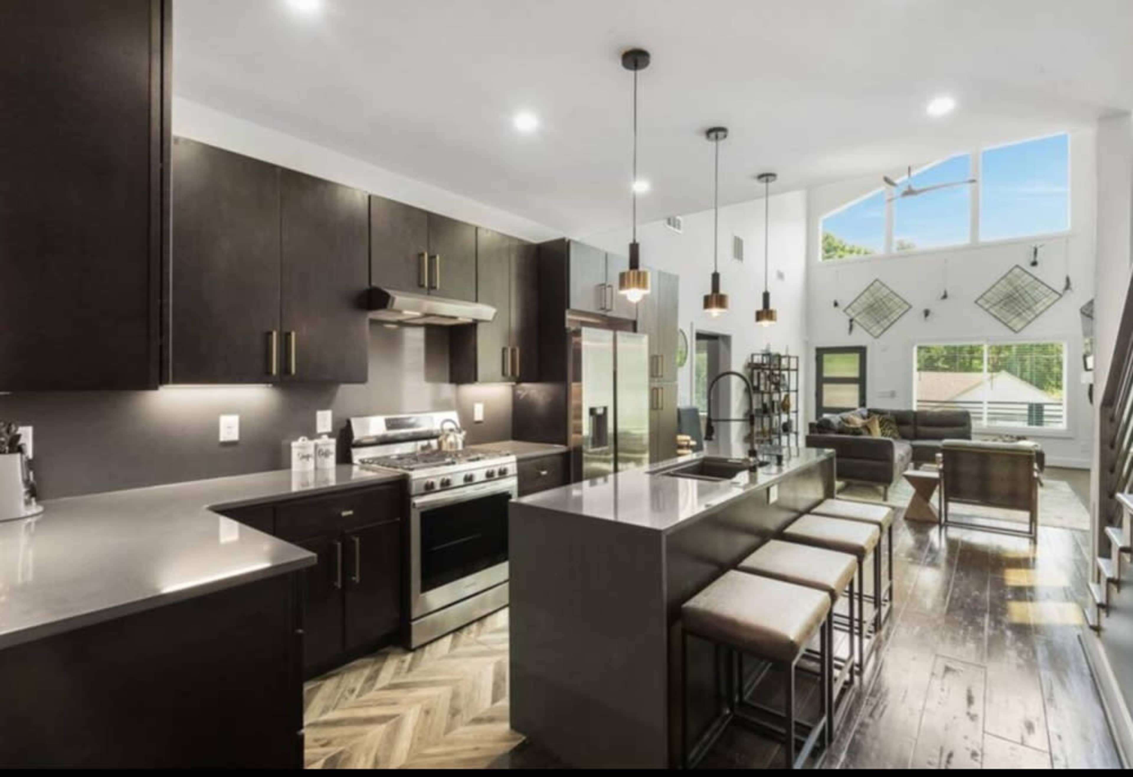 The image shows a modern kitchen featuring dark cabinetry, stainless steel appliances, and an island with bar seating.