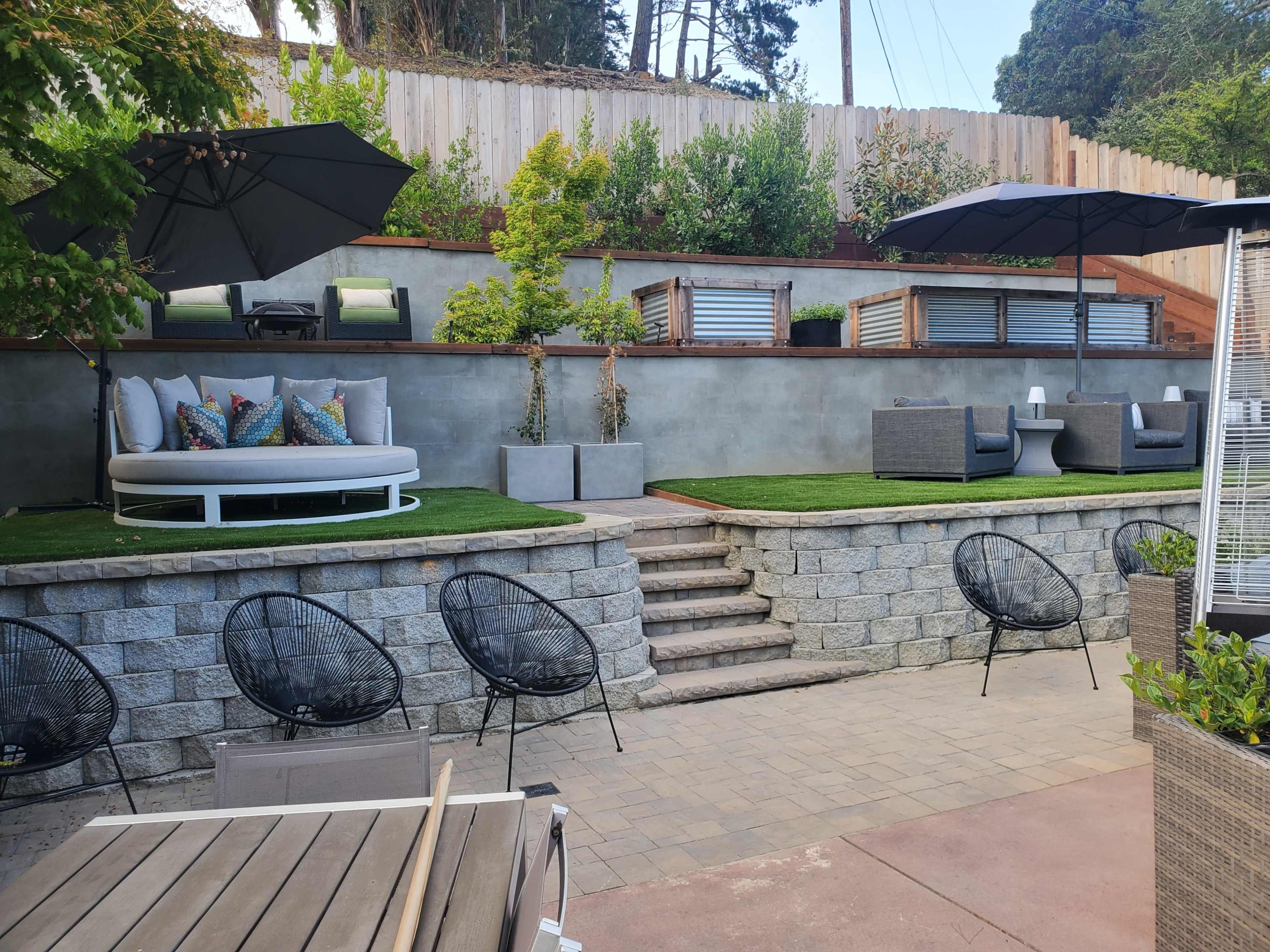 A backyard patio with tiered seating areas, lounge chairs, and landscaped greenery.