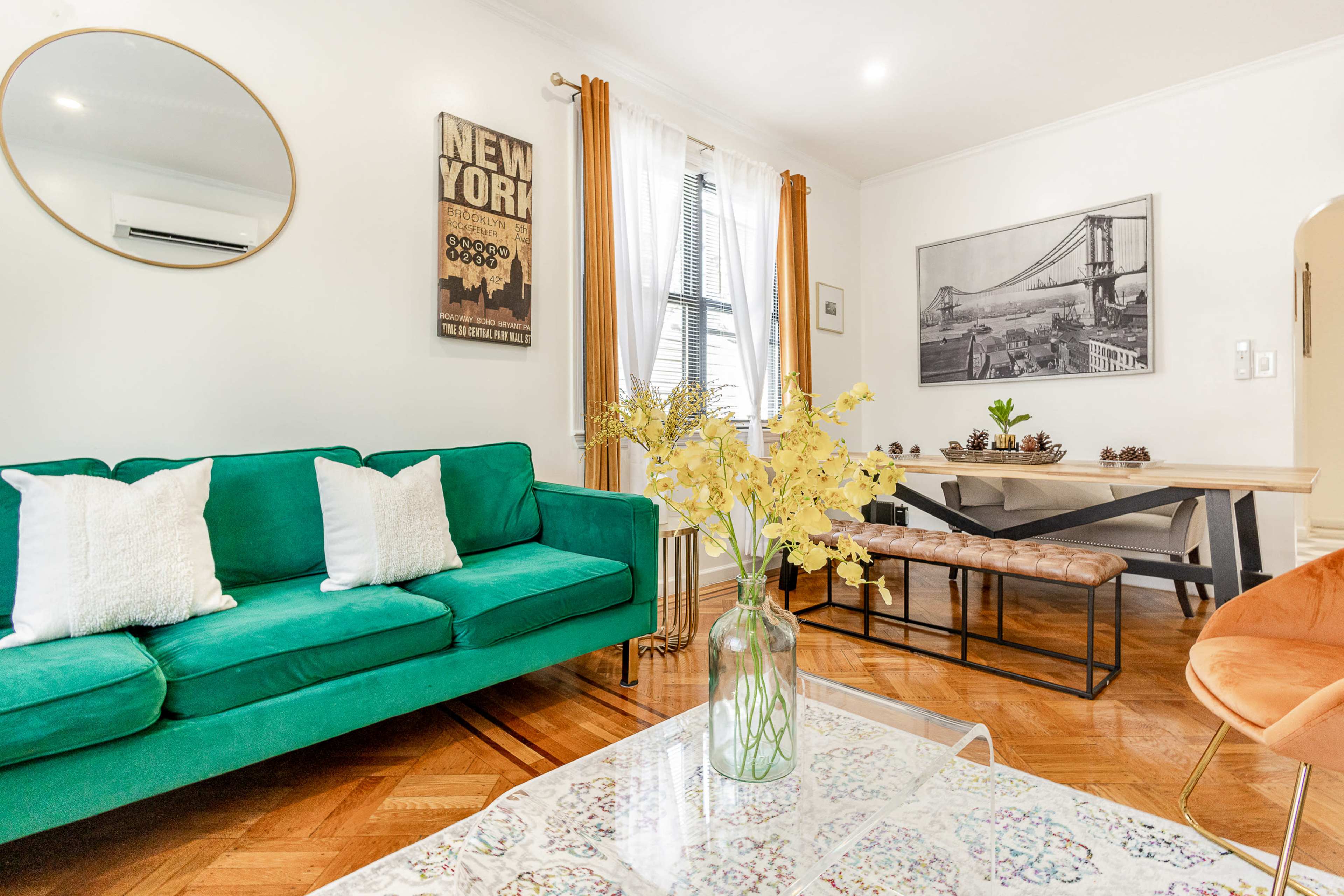A living room with a green couch, a wooden dining table, and decorative elements like a vase of flowers and framed artwork on the walls.